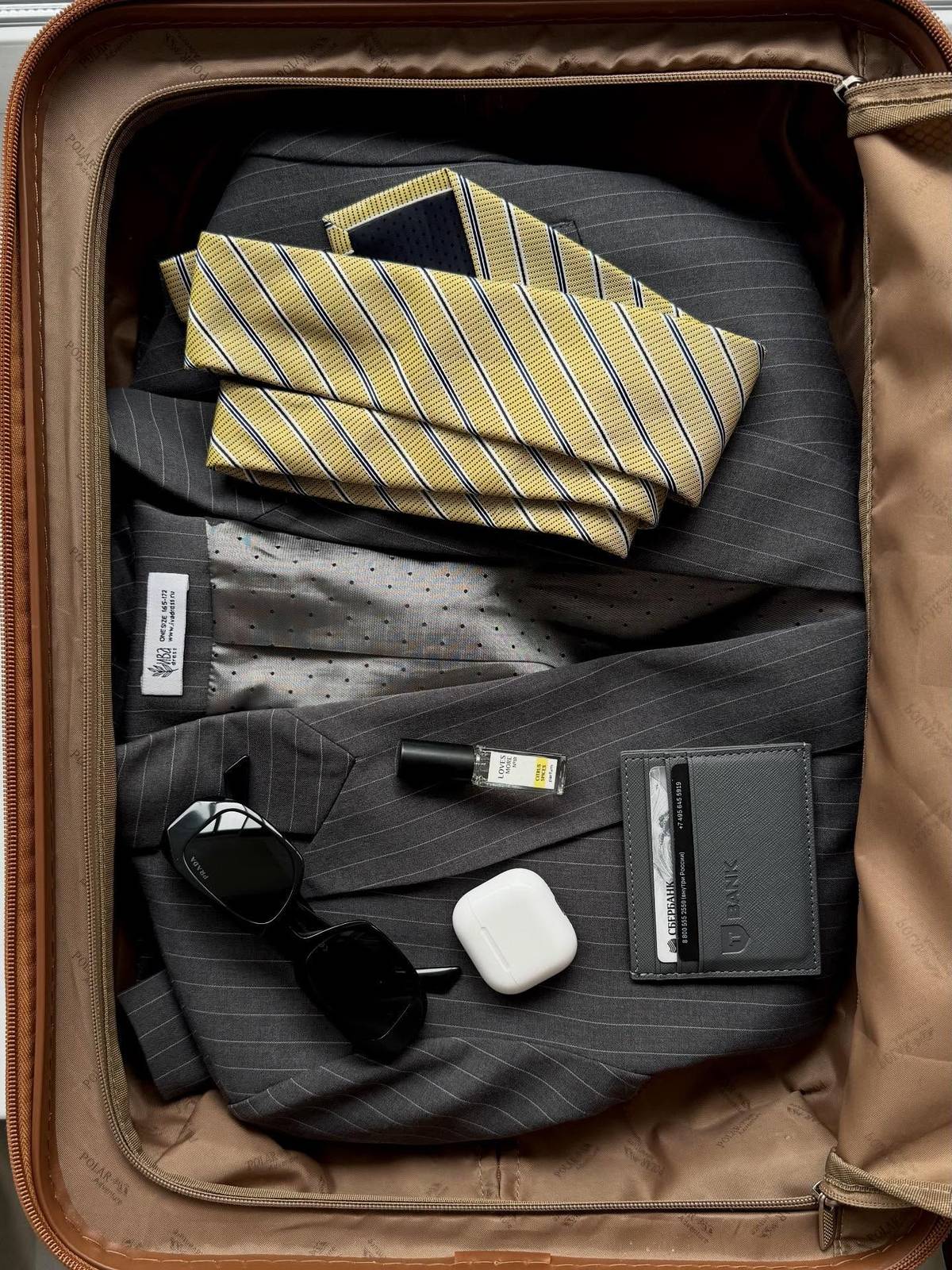 A suitcase packed with a striped tie, sunglasses and a leather wallet