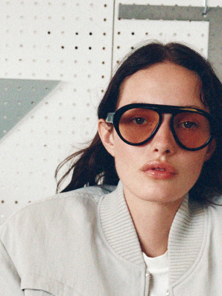 Model in a pale motorsport-inspired jacket and tinted sunglasses
