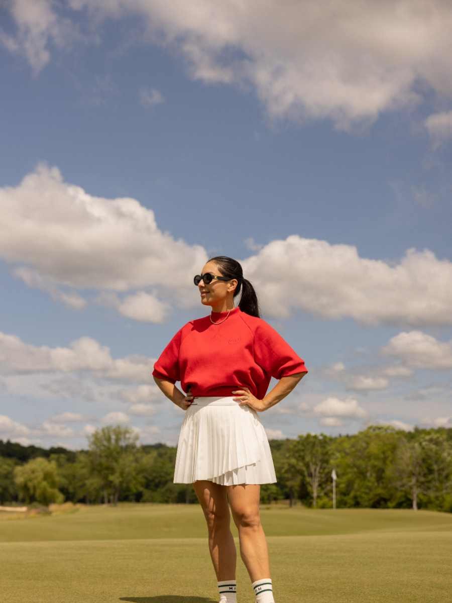 Woman in a red golf top and white skirt on a sunny course