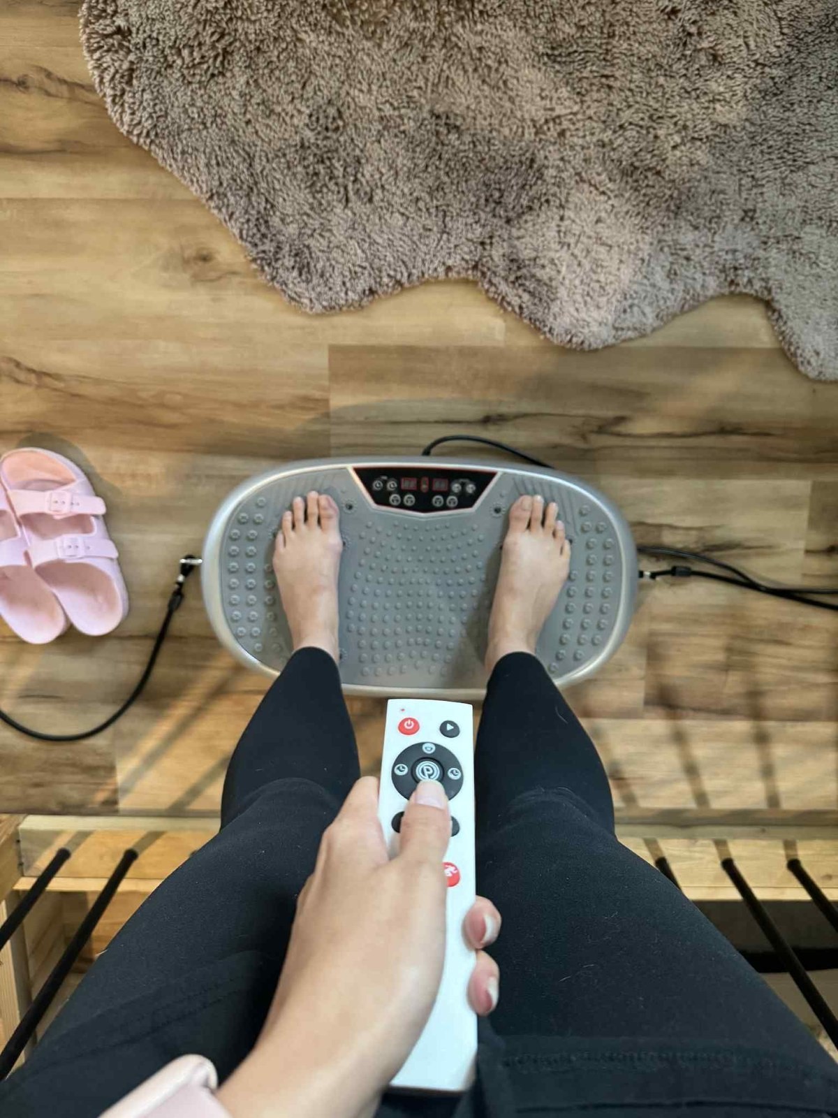Bare feet standing on a vibration plate with a remote control held below