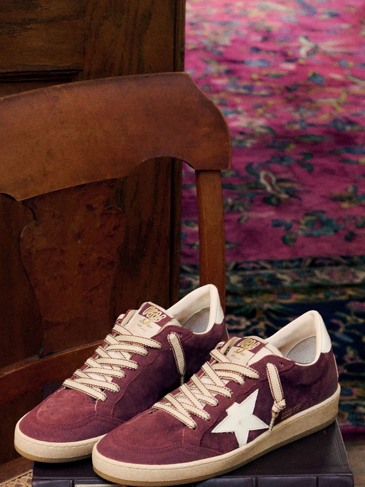 Burgundy suede Golden Goose Ball Star sneakers on a wooden chair above a patterned rug