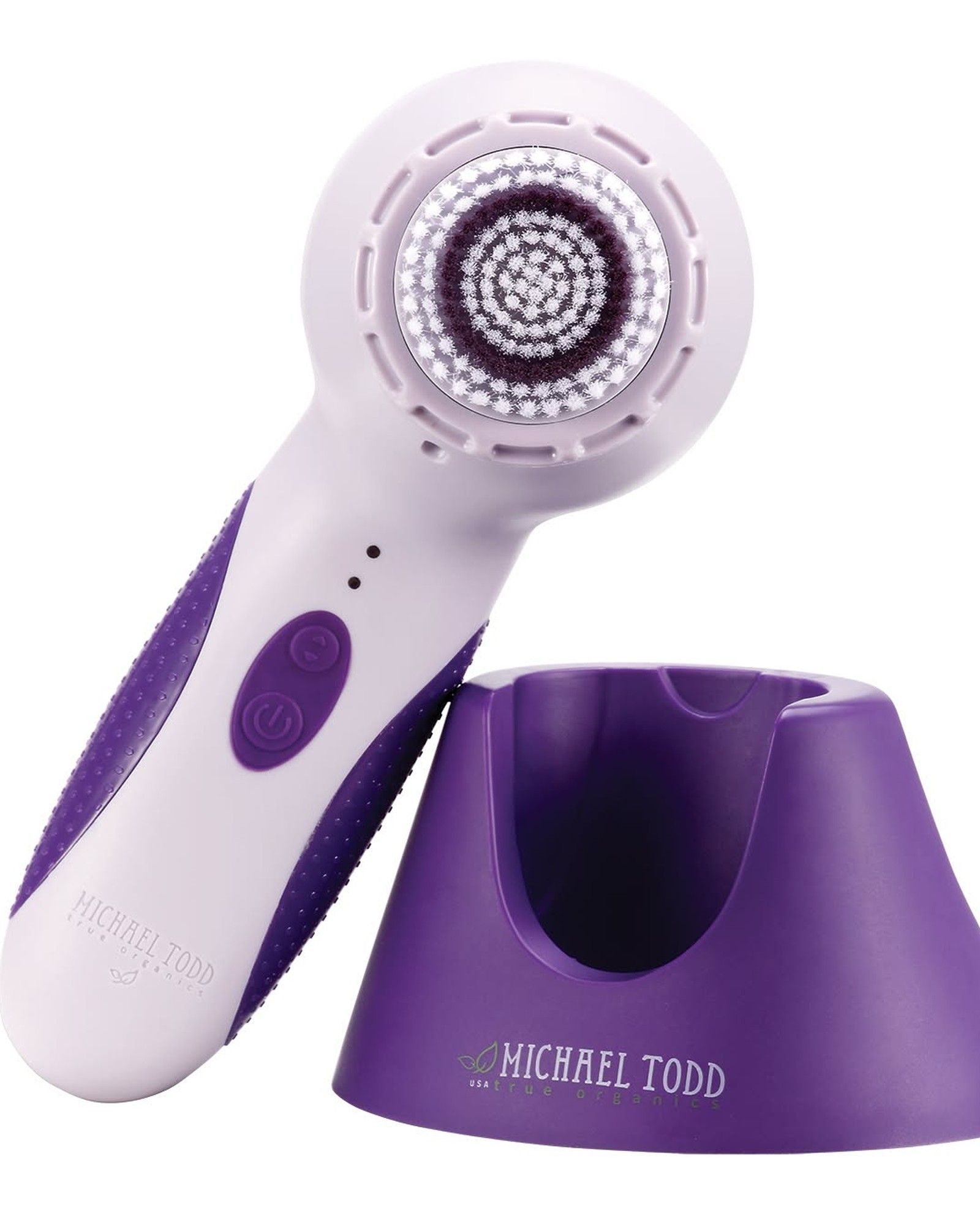 Lavender Michael Todd cleansing brush with purple grips and a round bristle head, resting beside its purple charging stand on a white background