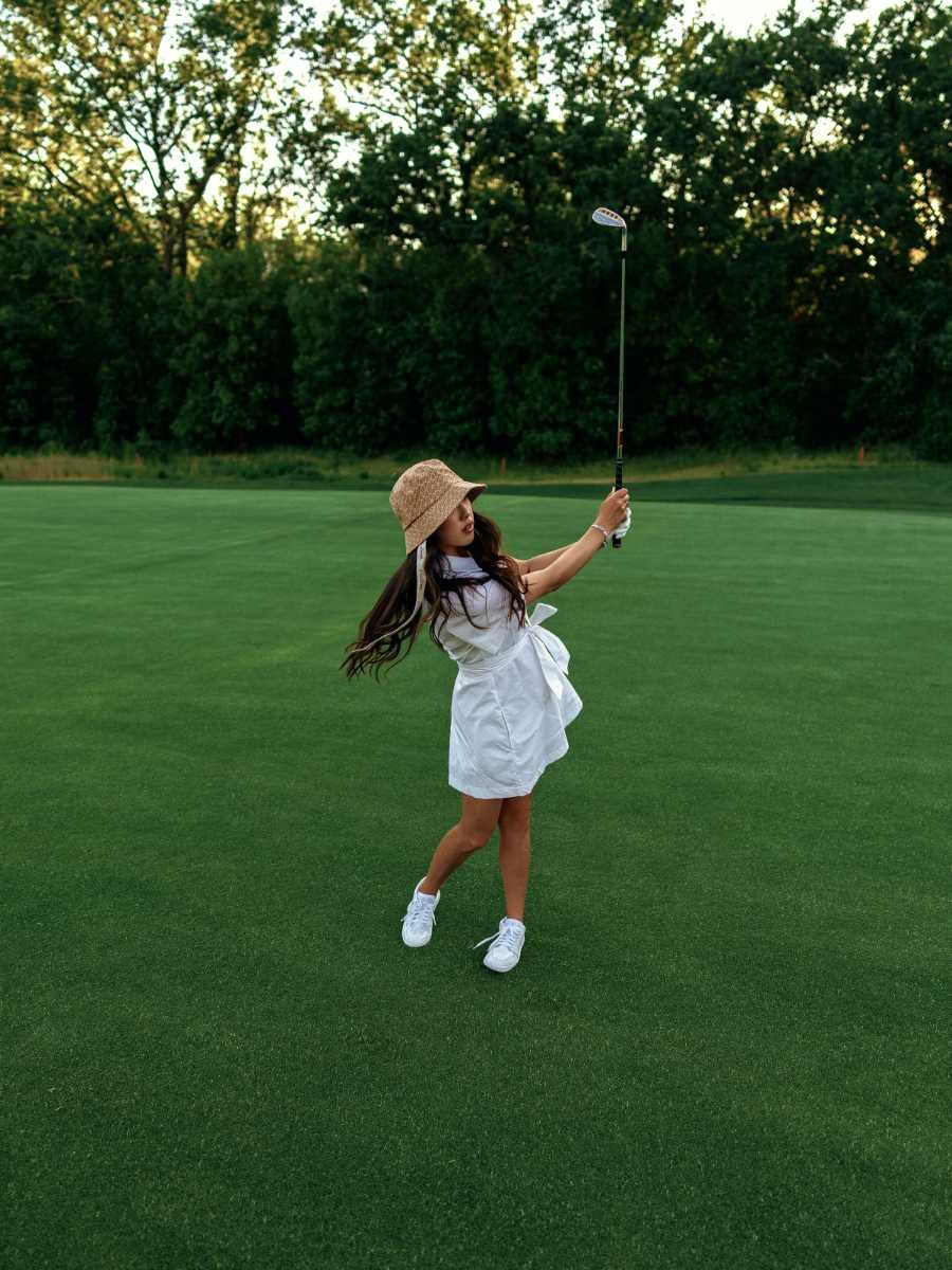 Malbon golfer swinging in a white dress on a green