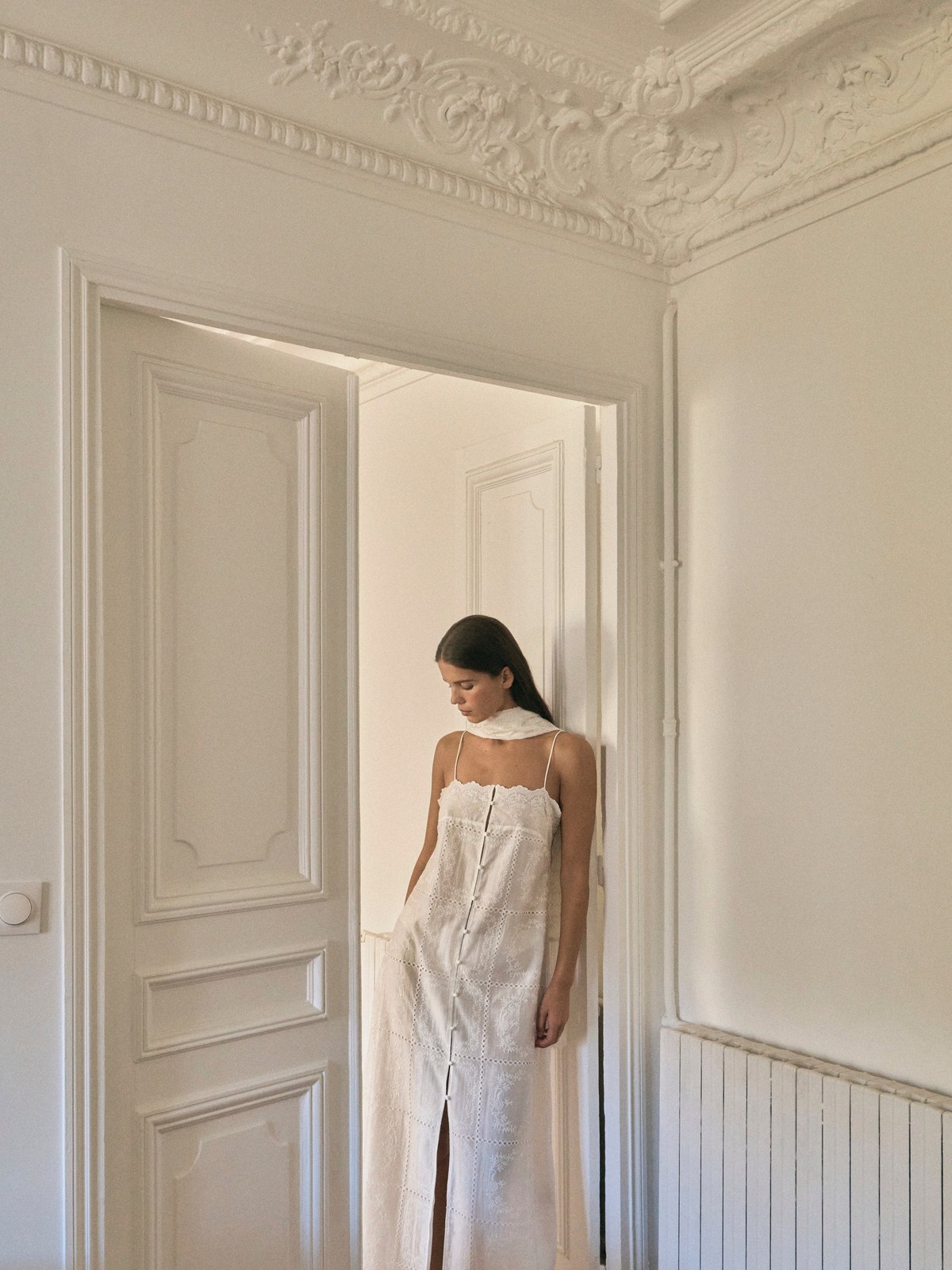 Model in an embroidered ivory dress standing in a pale townhouse doorway