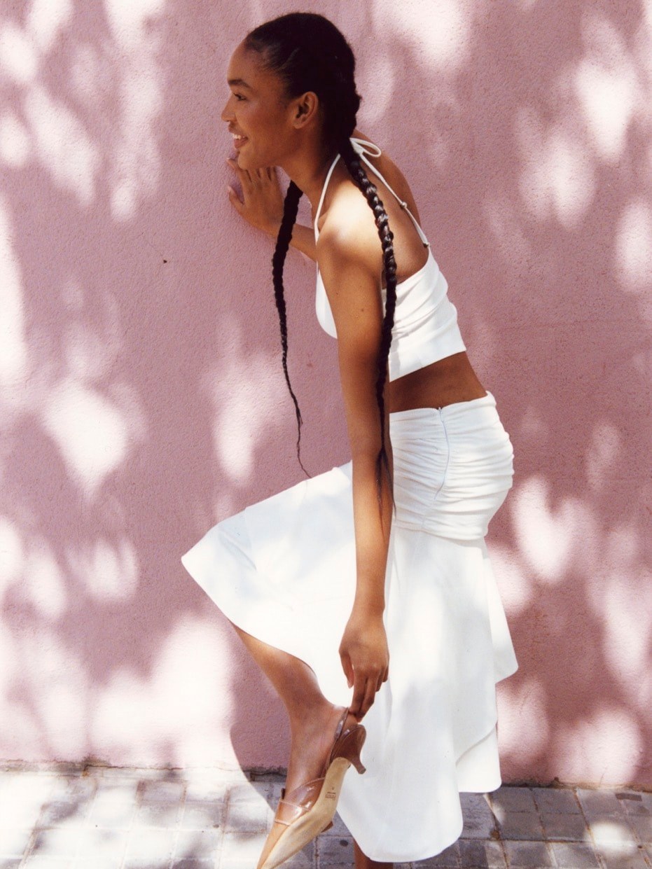 Feners campaign model in a white skirt against a sunlit pink wall