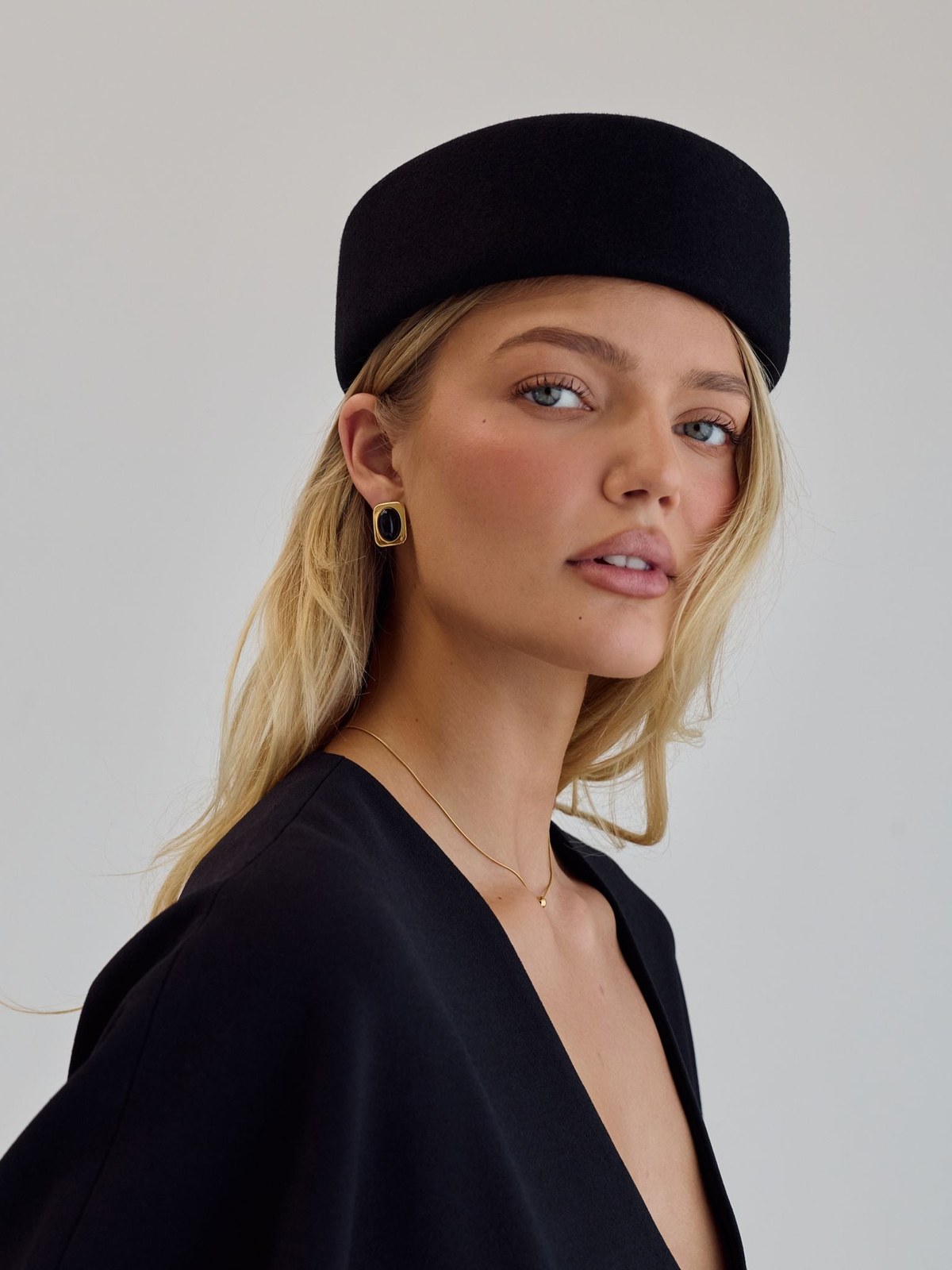 Blonde model in a black cap and top wearing Cendré earrings