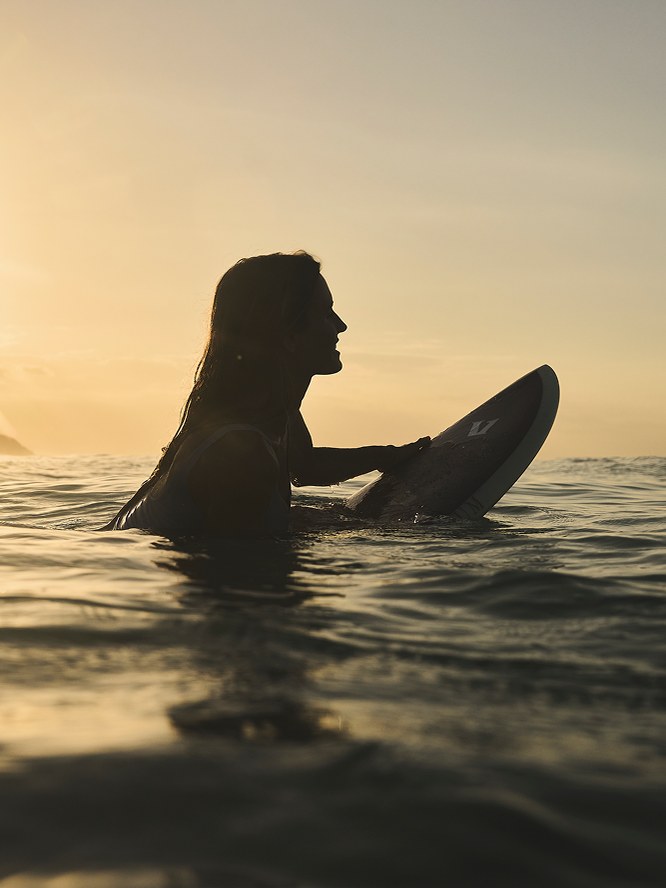 Surfer resting on a board in golden evening water
