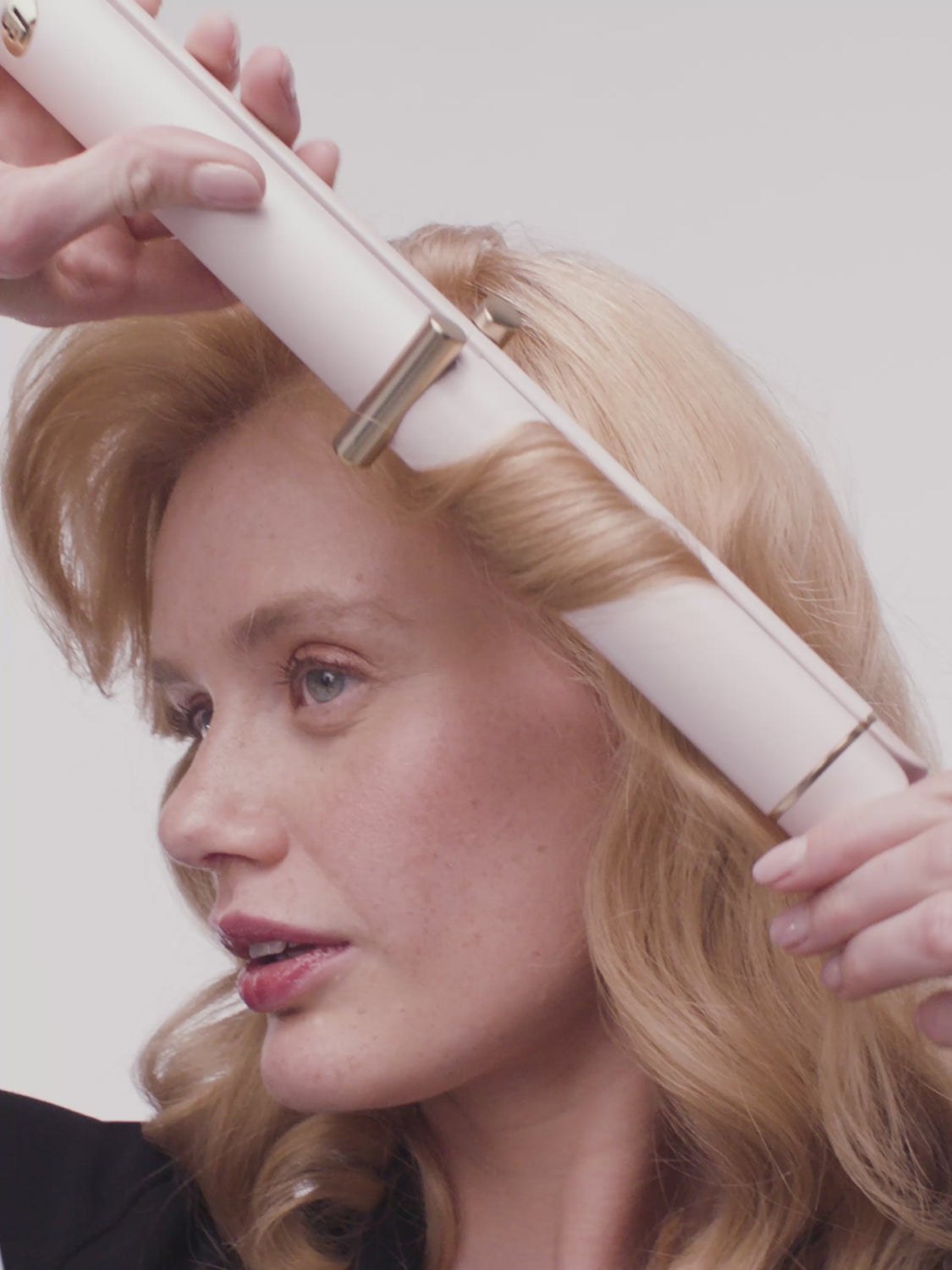 Red-haired model styling a section of hair with a white flat iron