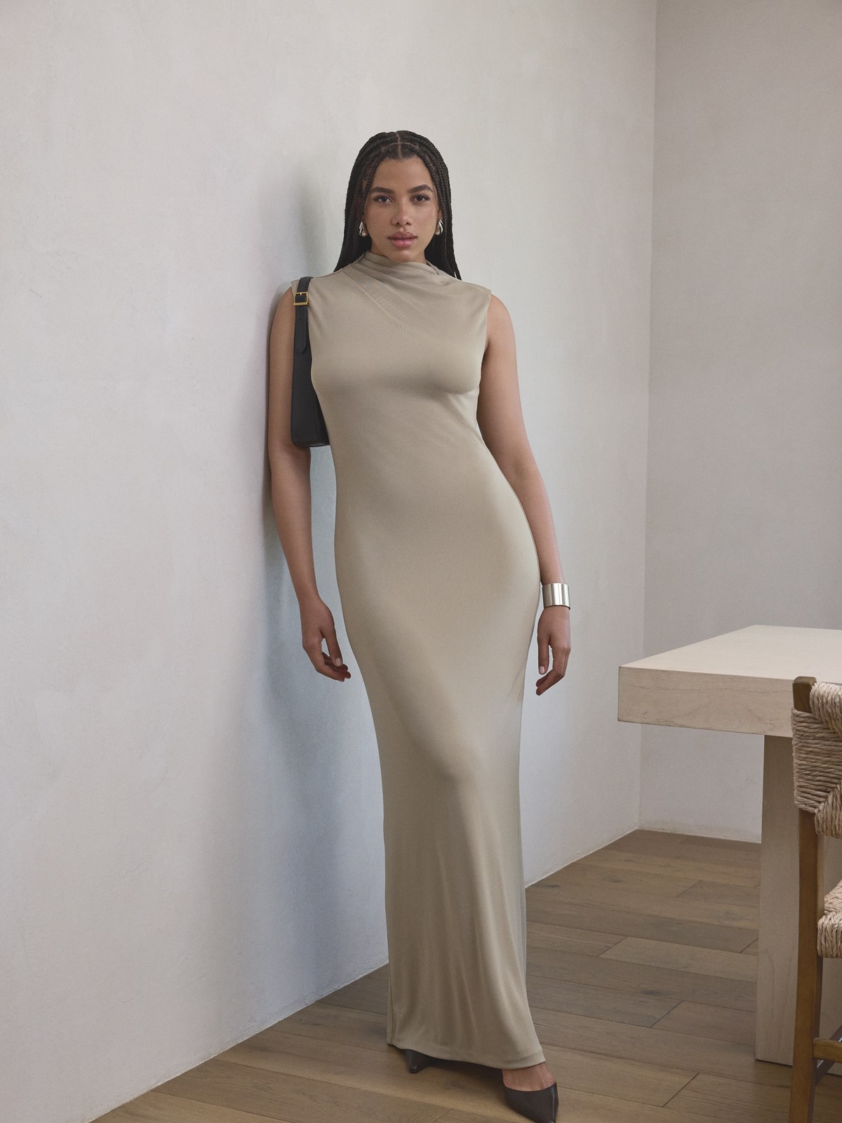 Model in a fitted taupe dress standing in a neutral interior