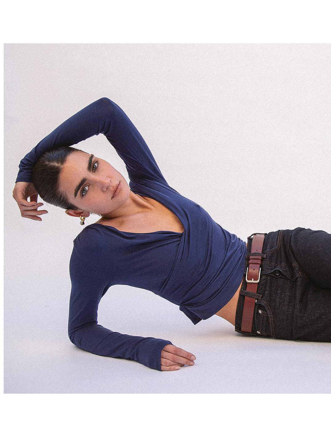 Model reclining in a navy top and dark jeans against a pale studio backdrop