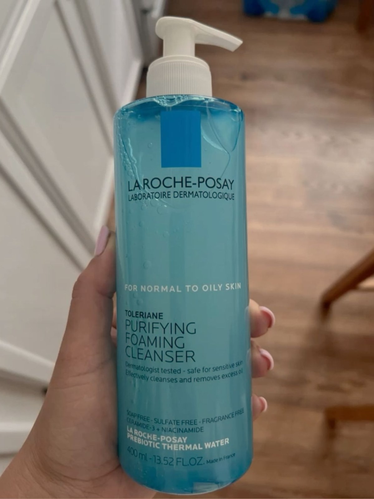 Hand holding a bottle of La Roche-Posay Toleriane Purifying Foaming Cleanser in a bathroom