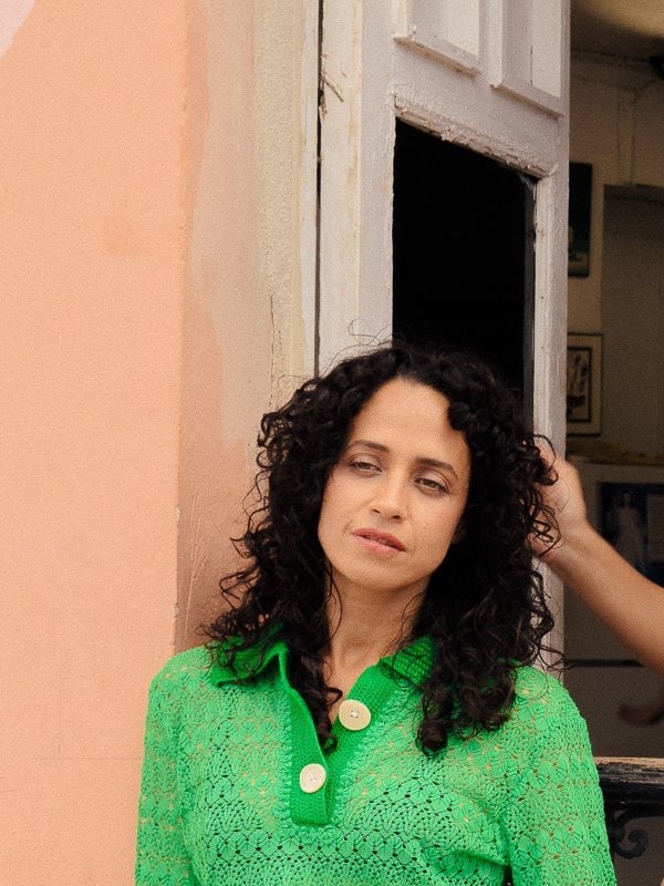 A curly-haired woman in a green knit top beside a pink doorway in Ceremonia's El Pelo Malo No Existe campaign.