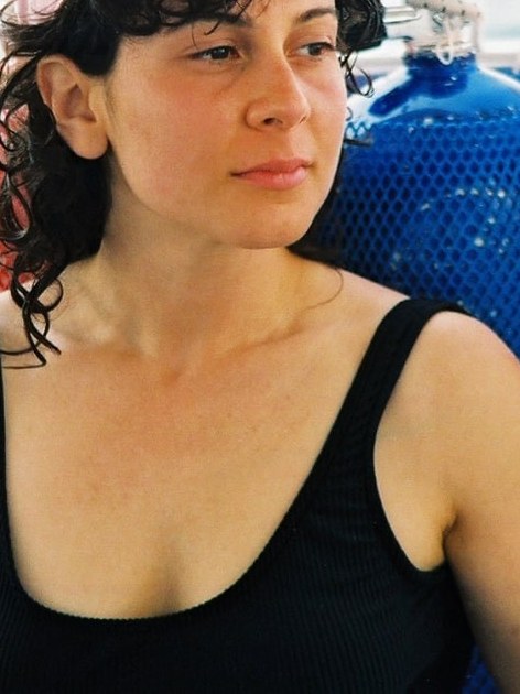 Woman seated on a boat in a black swimsuit with blue flotation gear behind her