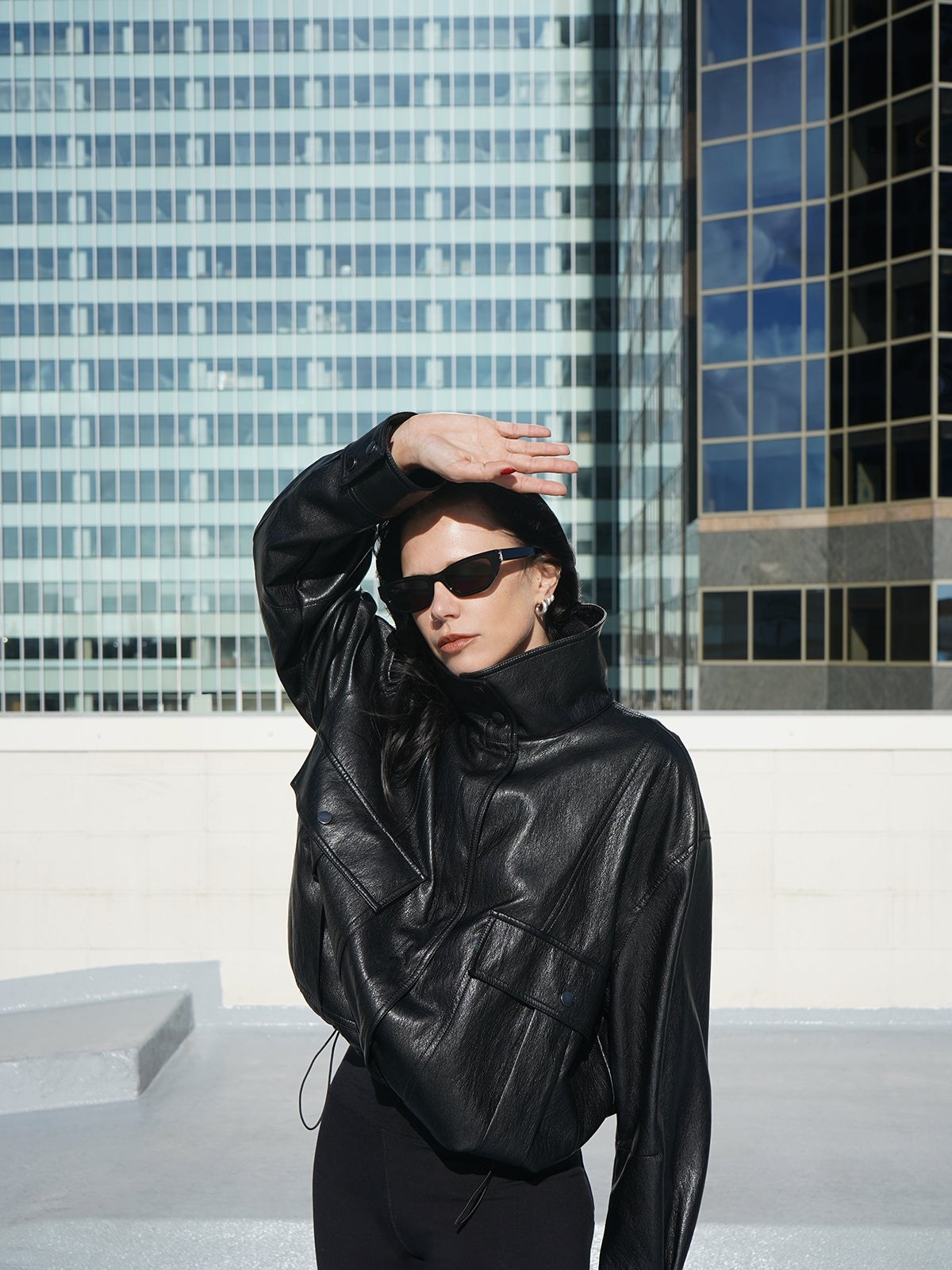 Model in a black leather-look jacket on a rooftop with city windows behind her