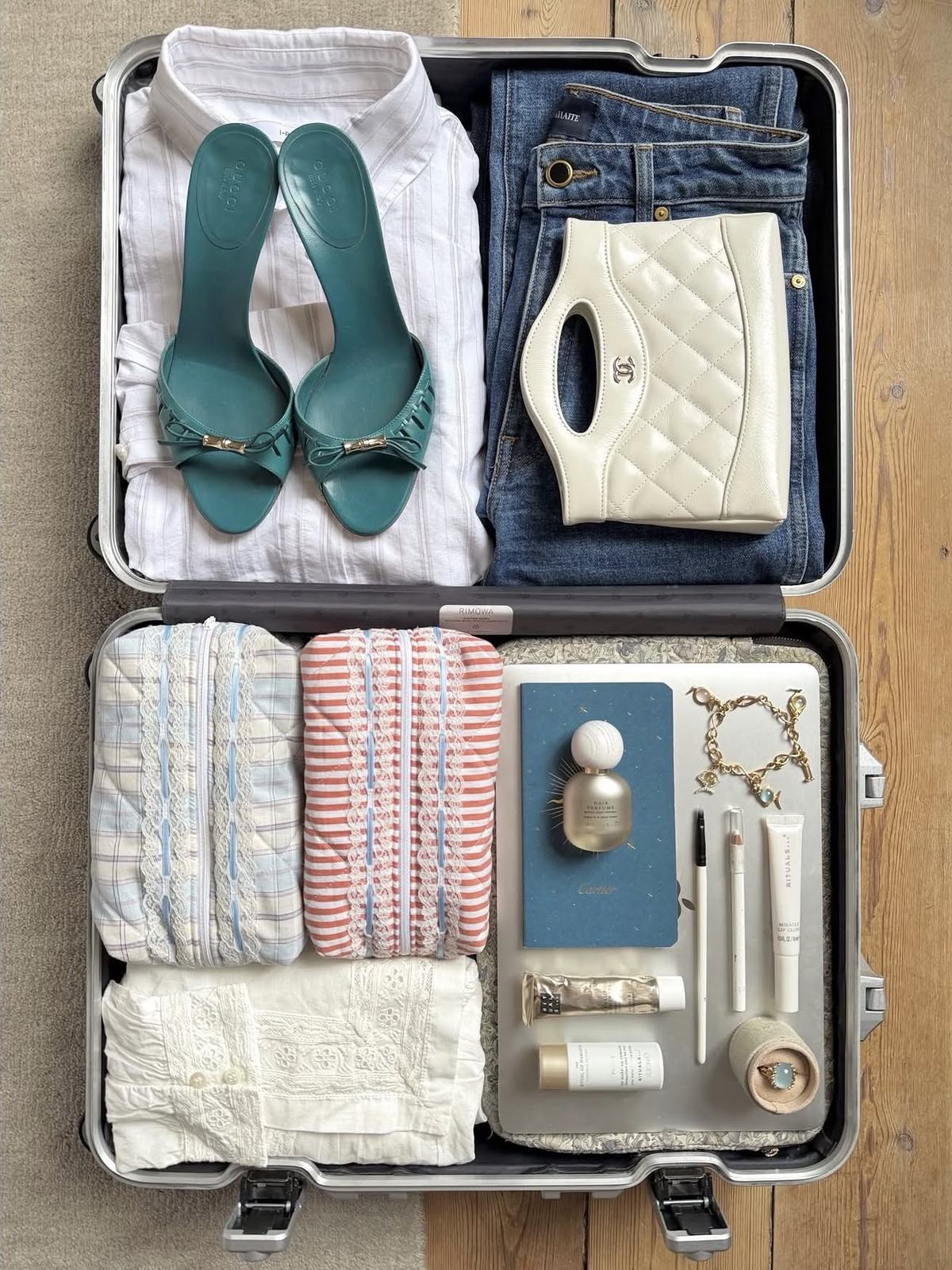A suitcase packed with teal heels, a cream bag and folded linens