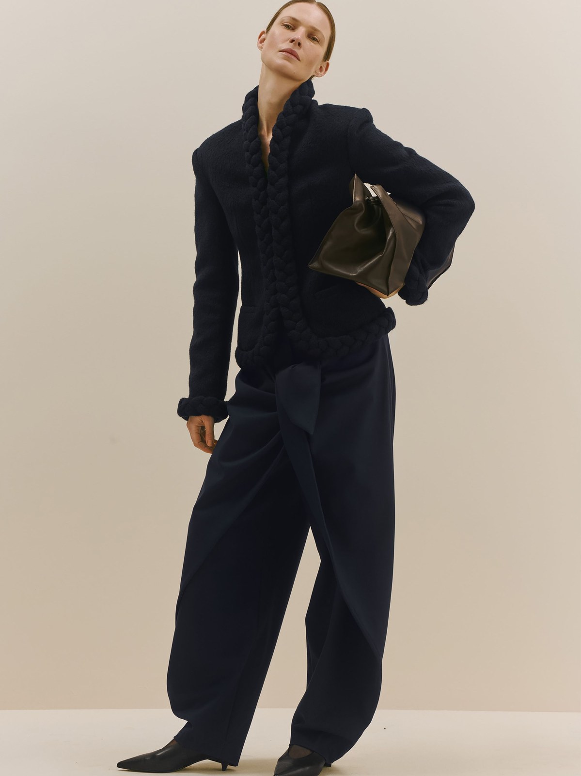 Model in a dark tailored suit and carrying a structured bag for Bevza Fall 2026