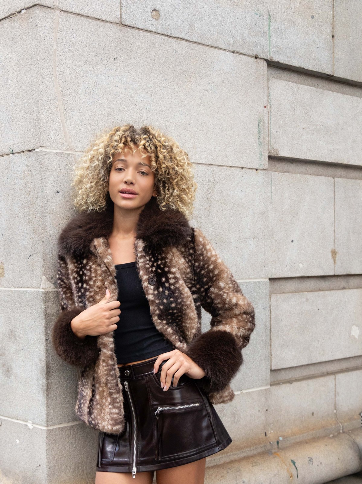 Model in a plush brown jacket and leather skirt on a city sidewalk