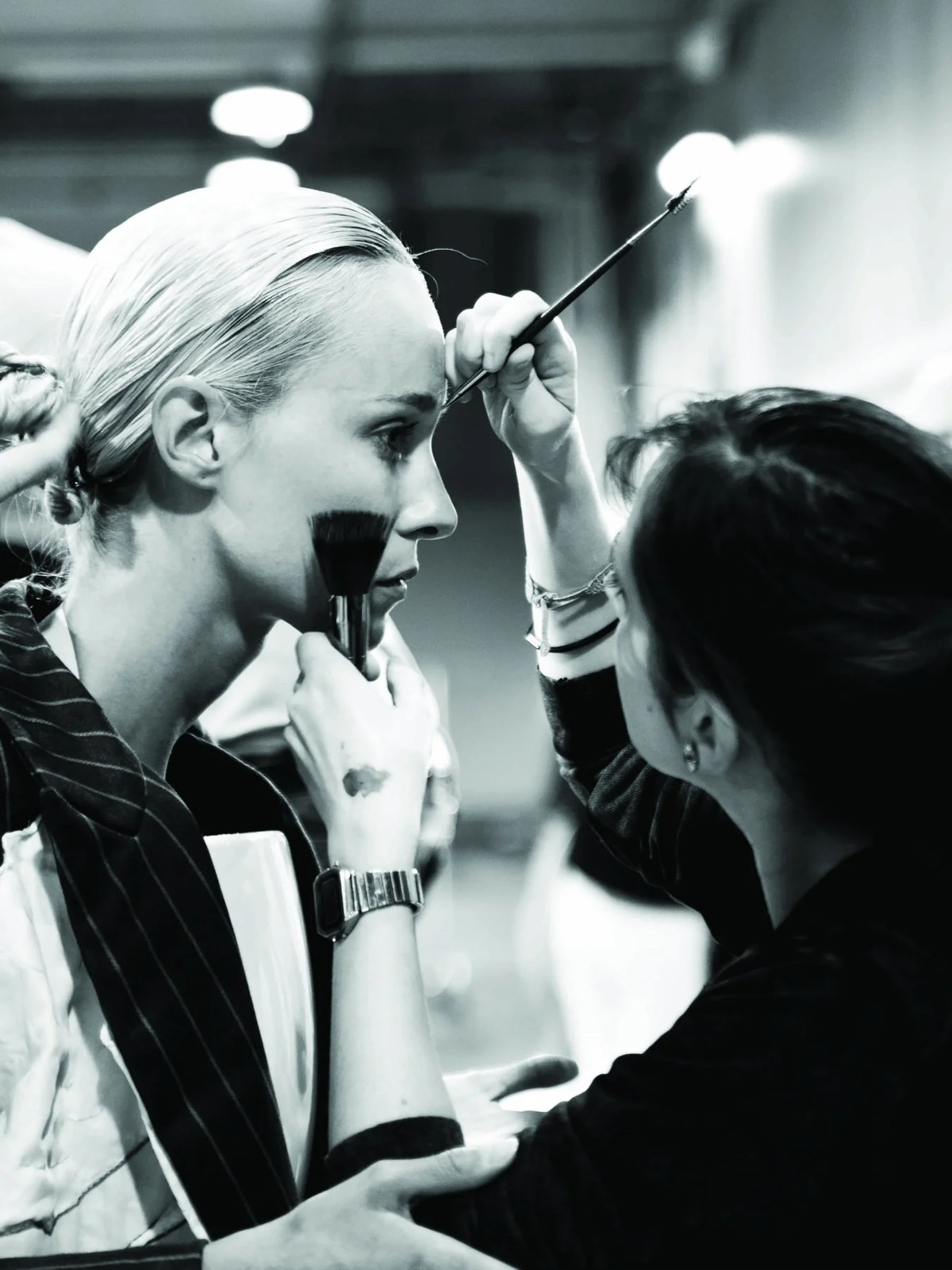 Black and white backstage shot of makeup artists working on a model