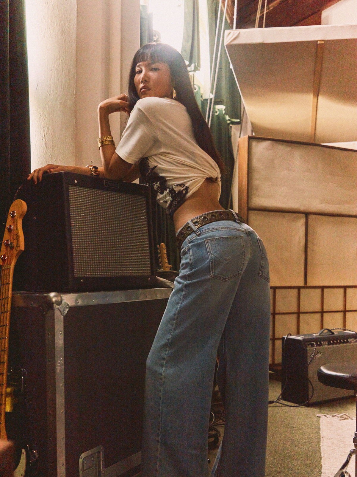 Model in light wash jeans posing beside an amplifier