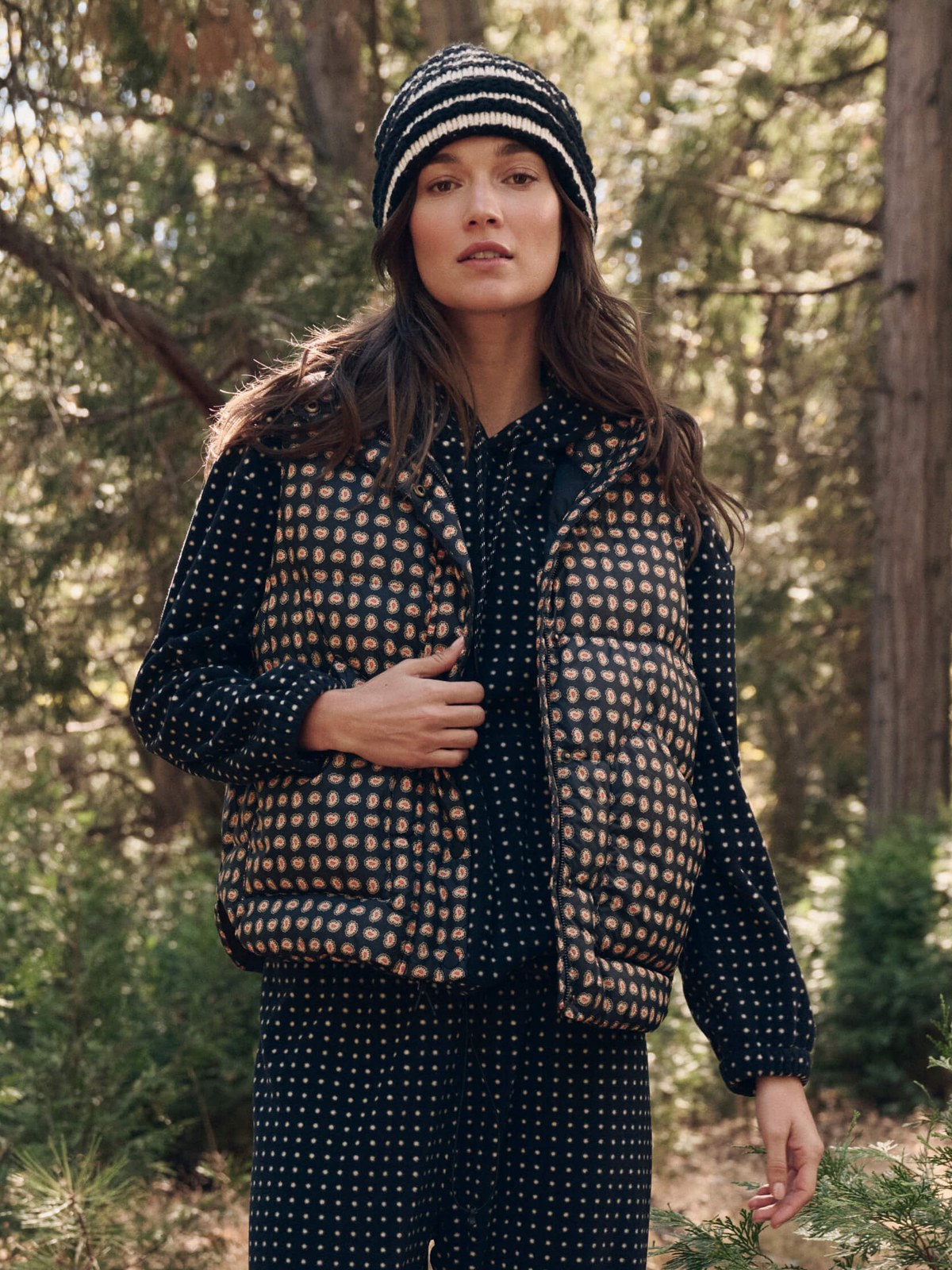 Model in a patterned set and knit hat standing in a forest