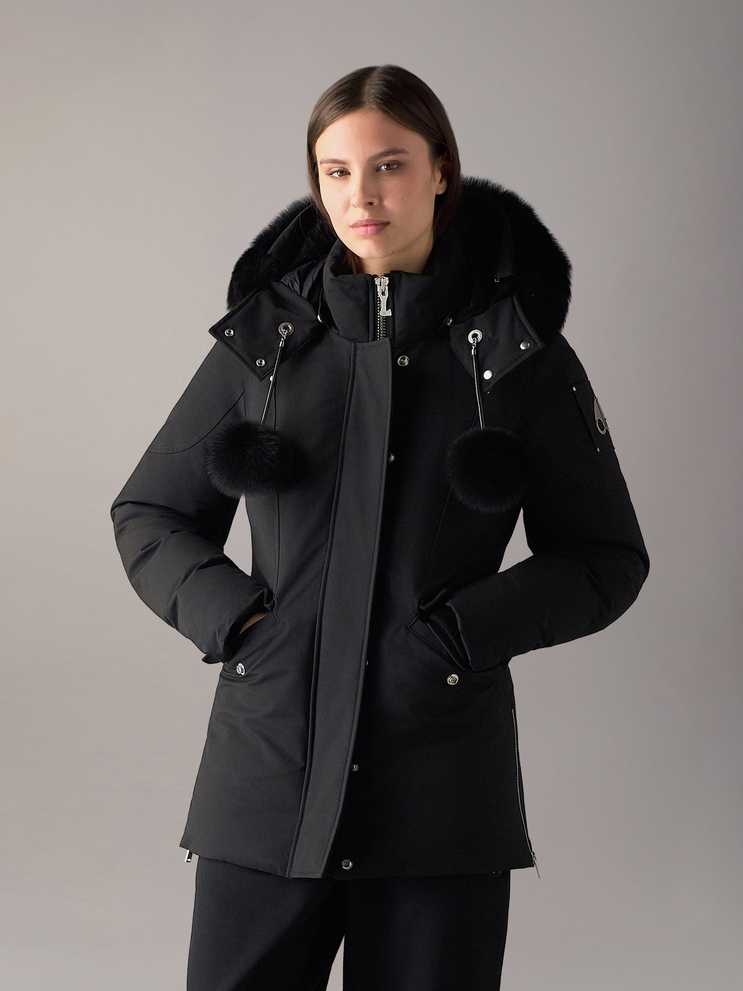 Model in a black parka with fur hood trim and pom poms