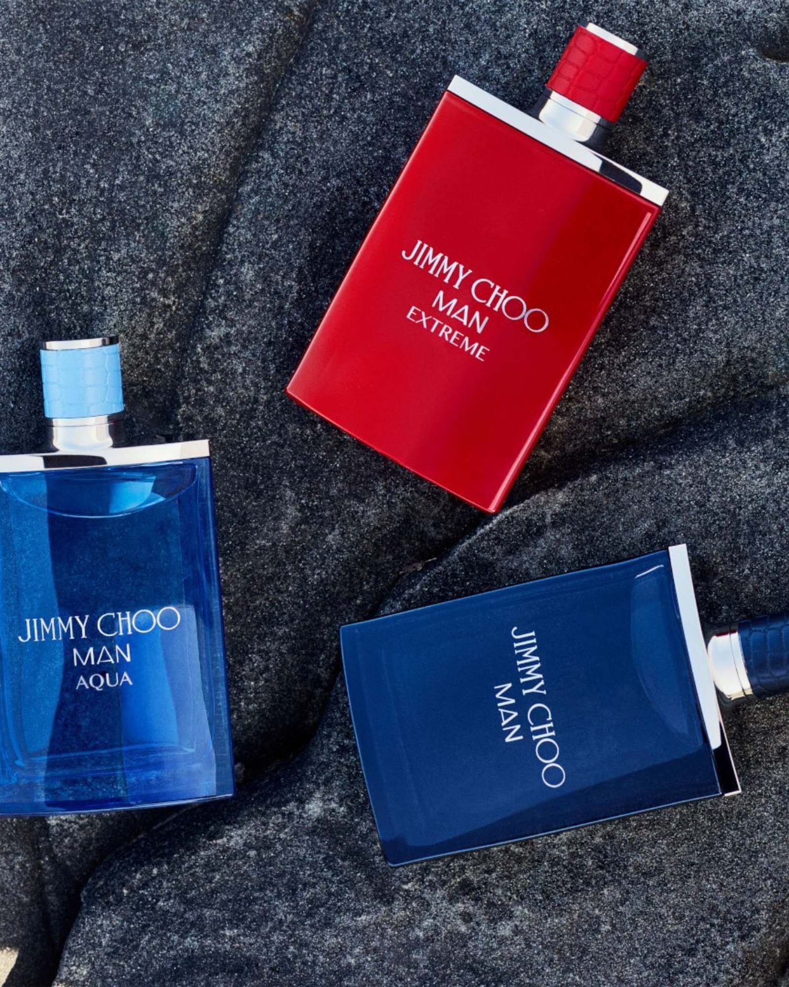Jimmy Choo Man Aqua, Man Extreme and Man bottles in blue and red lying on dark grey stone