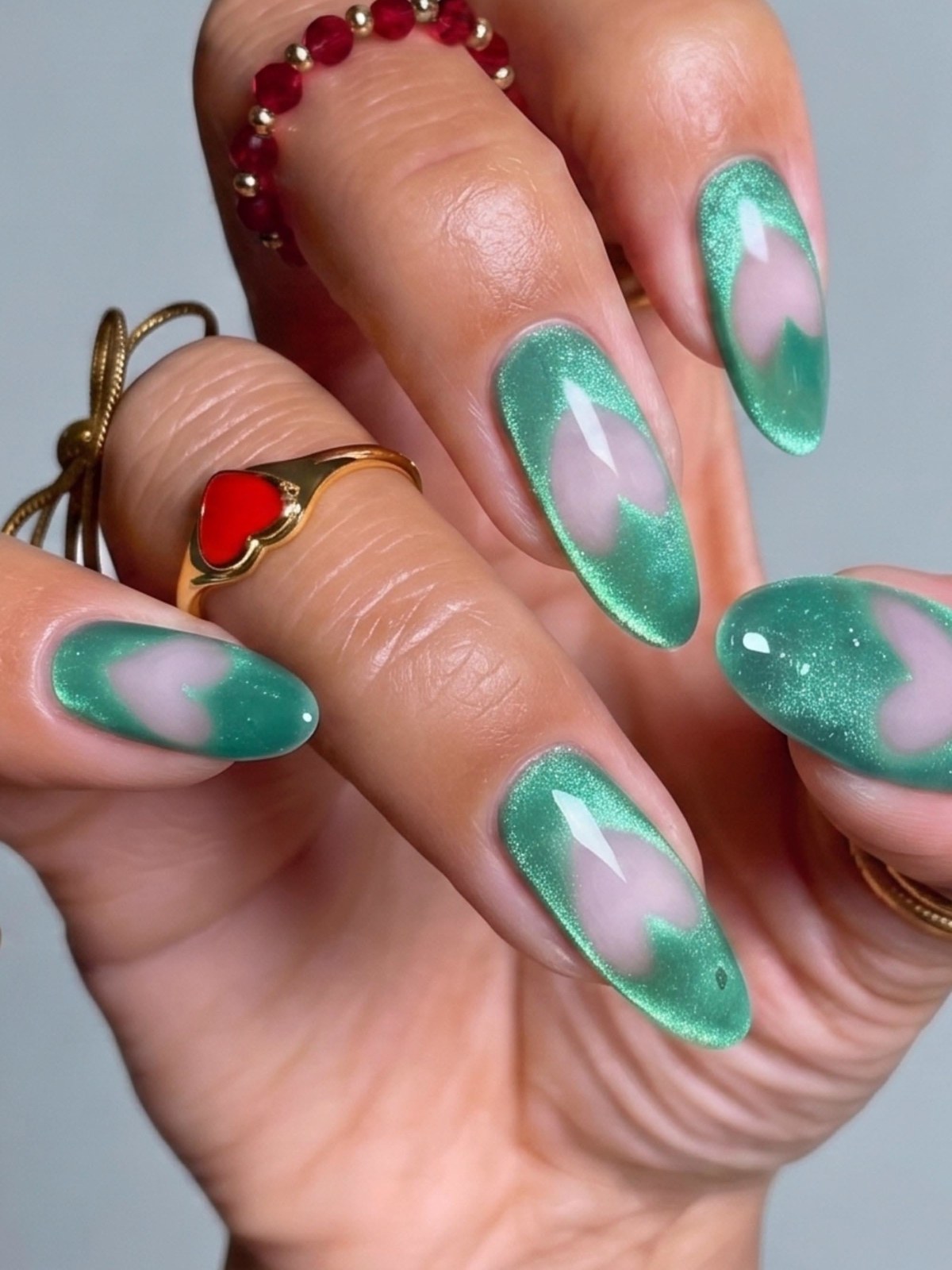 Green aura almond nails with glitter tips and a red stone ring