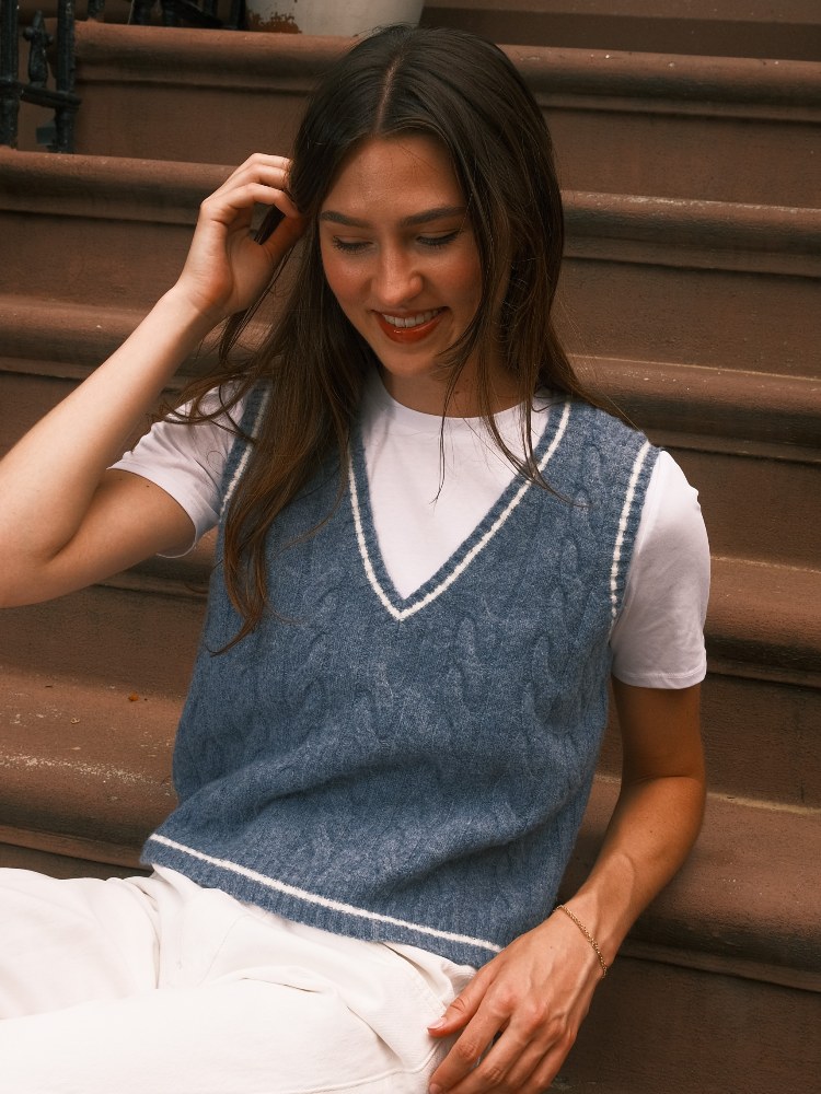 Model in a grey knit vest seated on city steps