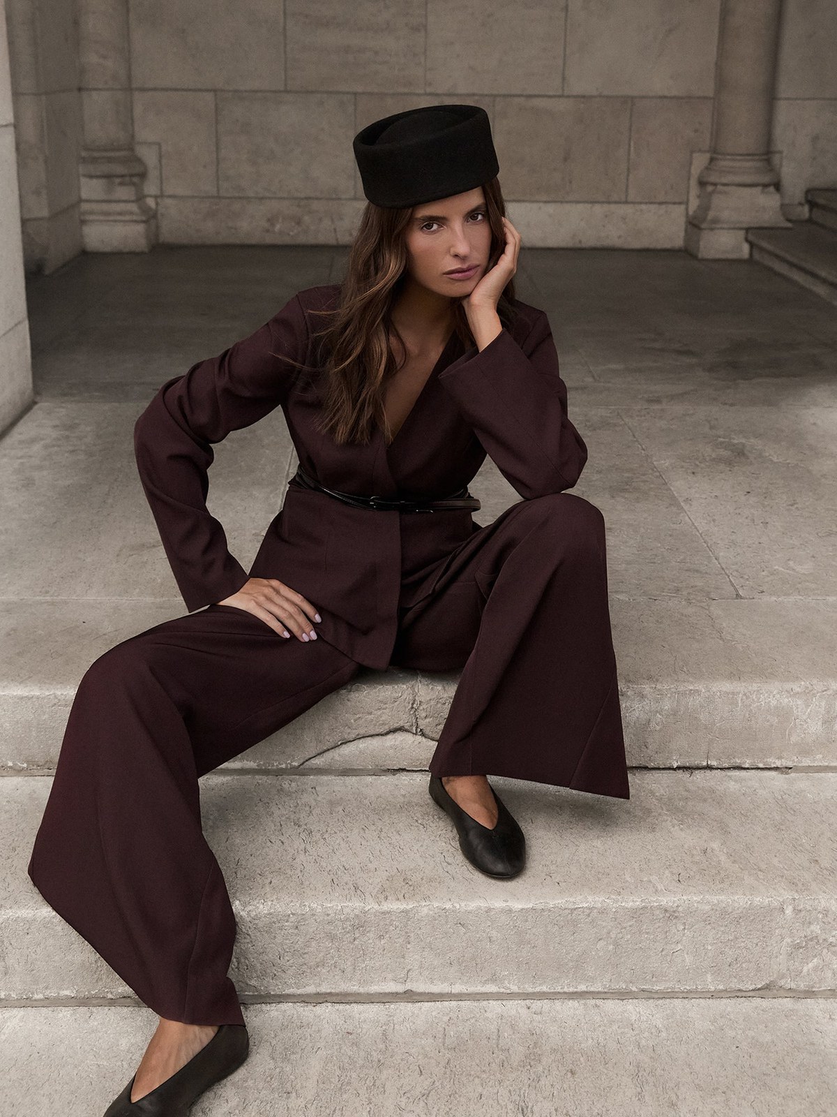 Model in a plum suit and cap seated on stone steps