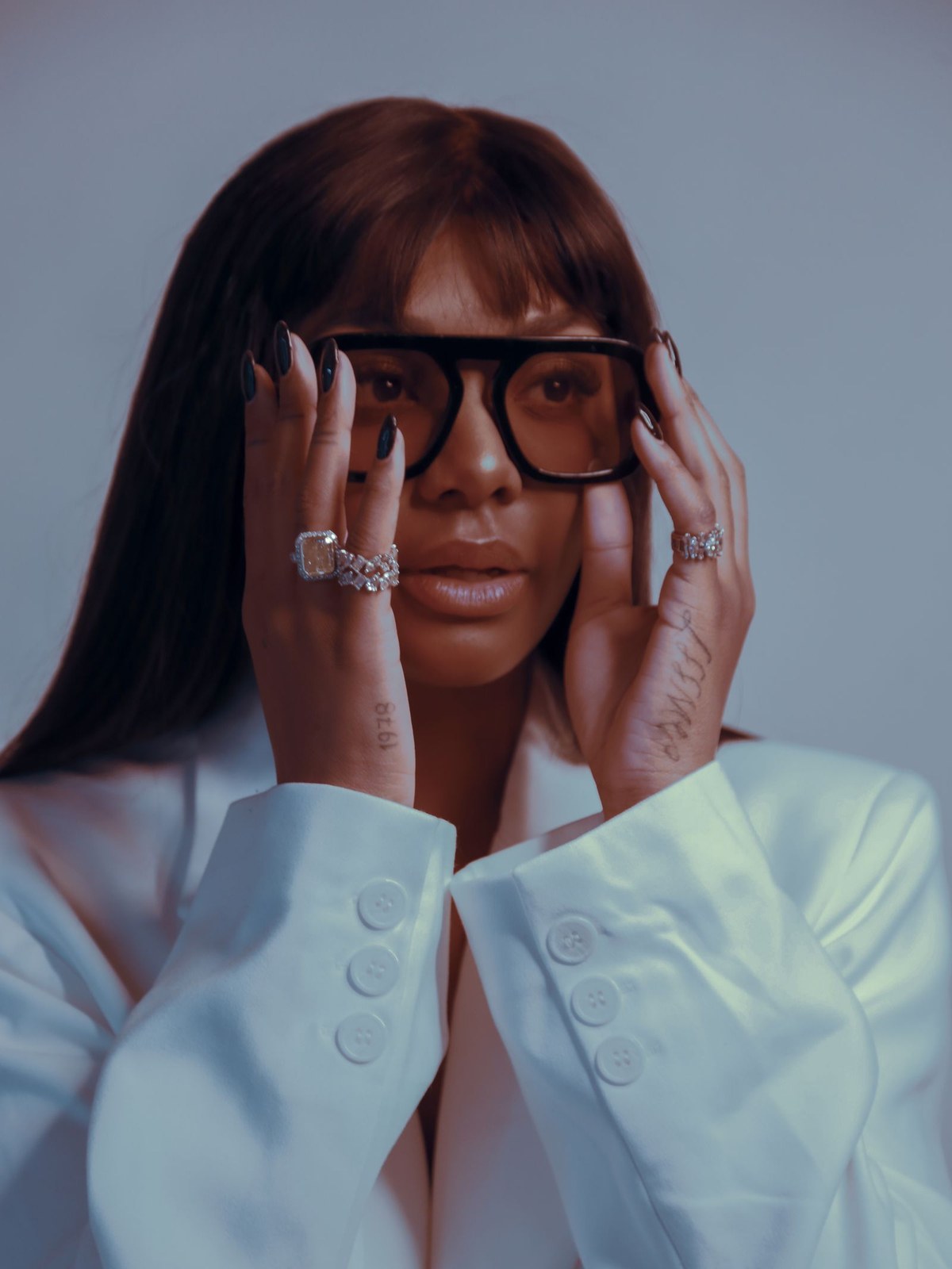 Model in statement black eyewear and a pale blue coat against a cool backdrop