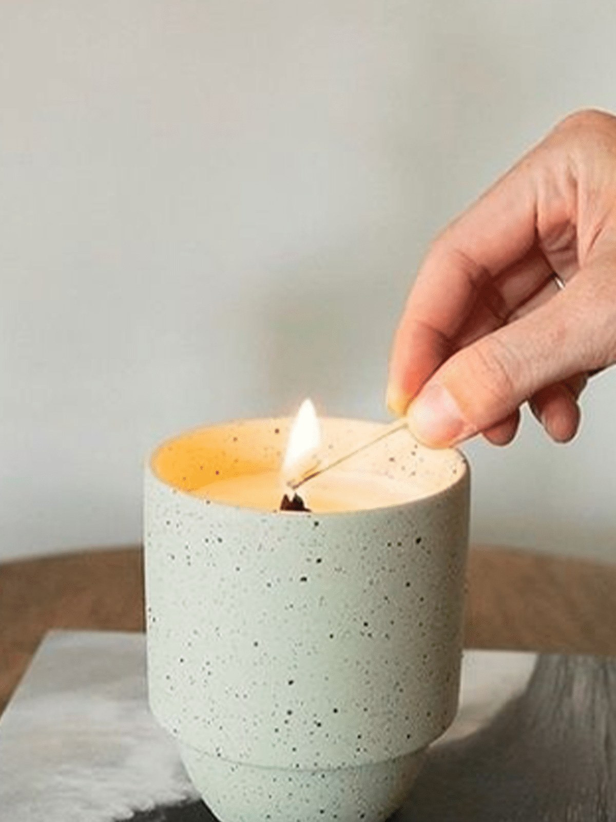 Hand lighting a speckled candle on a tabletop