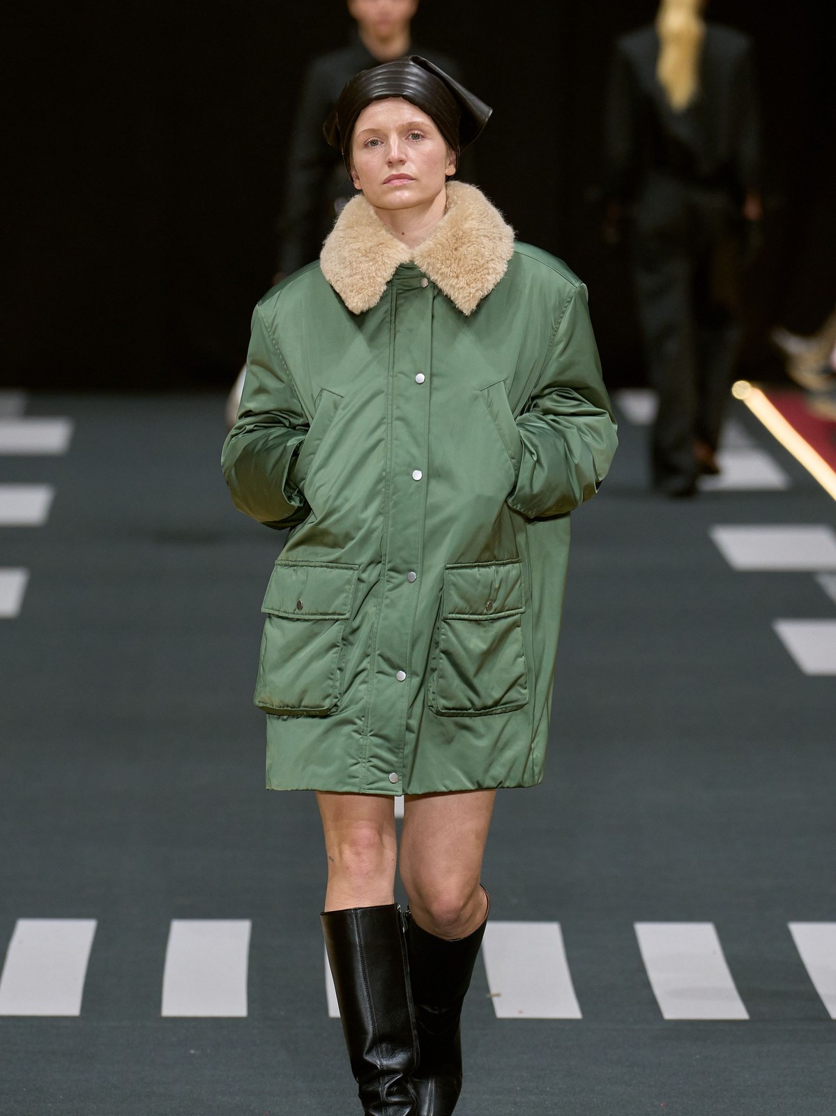 Runway model in a green padded coat with a light shearling collar and cuffs
