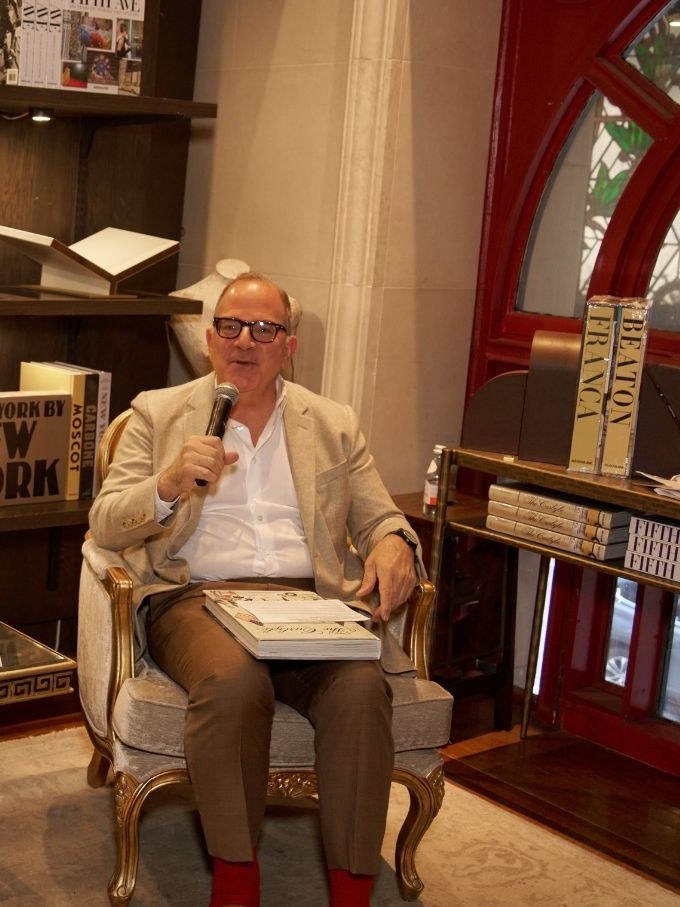 An author speaks with a microphone beside books at an Assouline event.