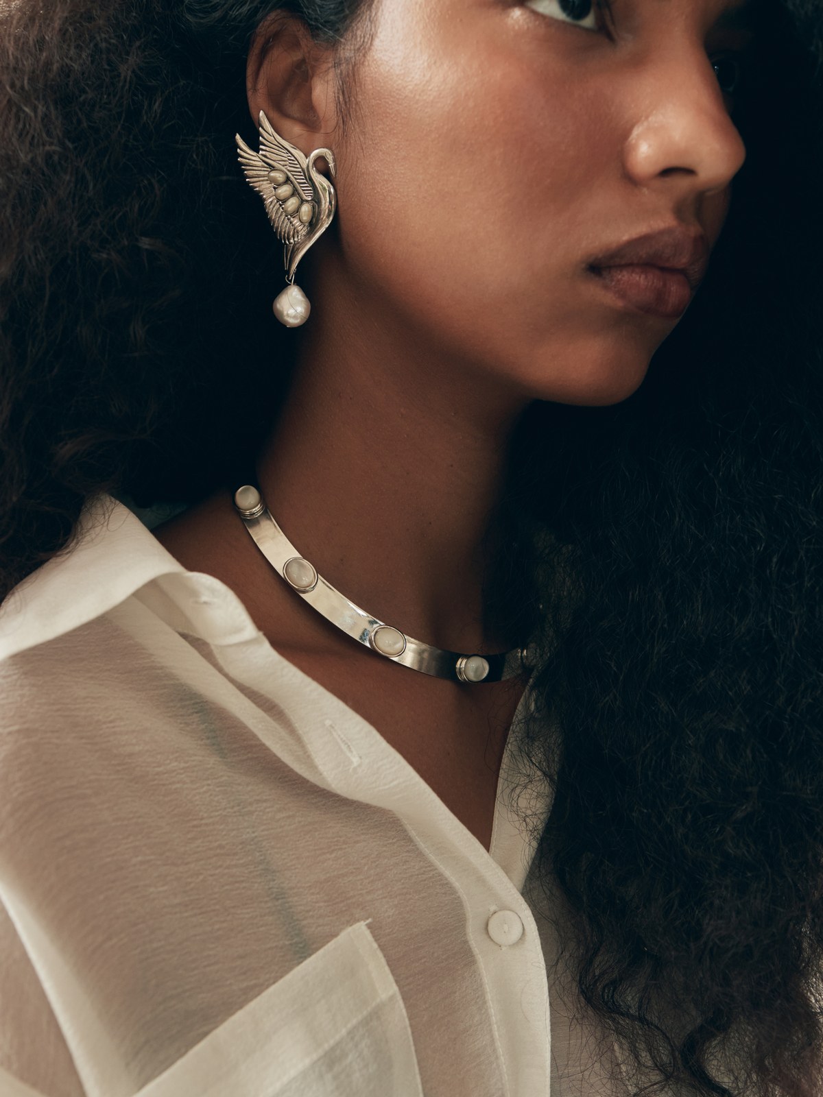 Close-up of a model wearing sculptural wing earrings and a silver necklace