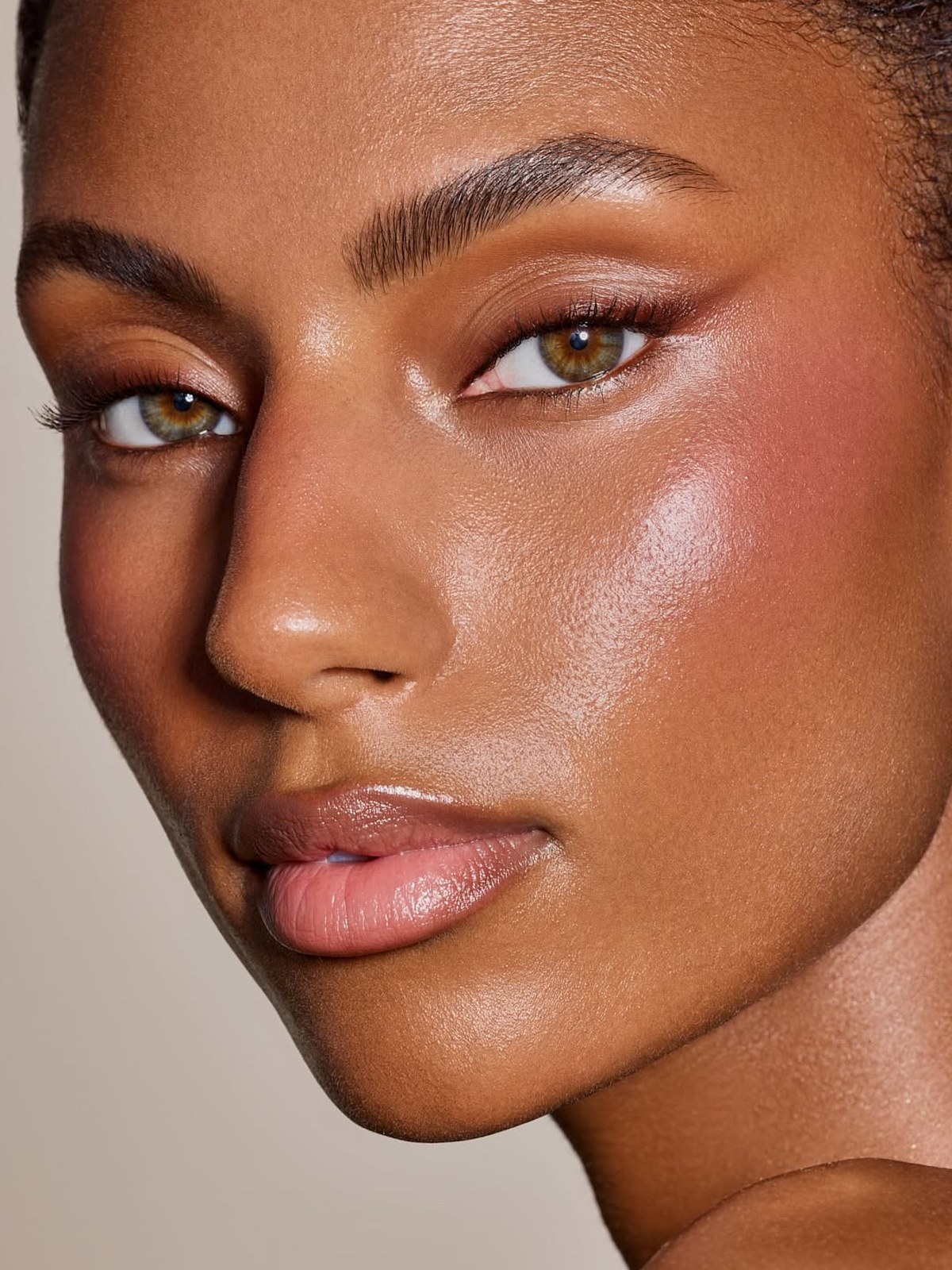 Close-up of a woman with a deep skin tone, glowing radiant skin, rosy blush and a nude pink lip