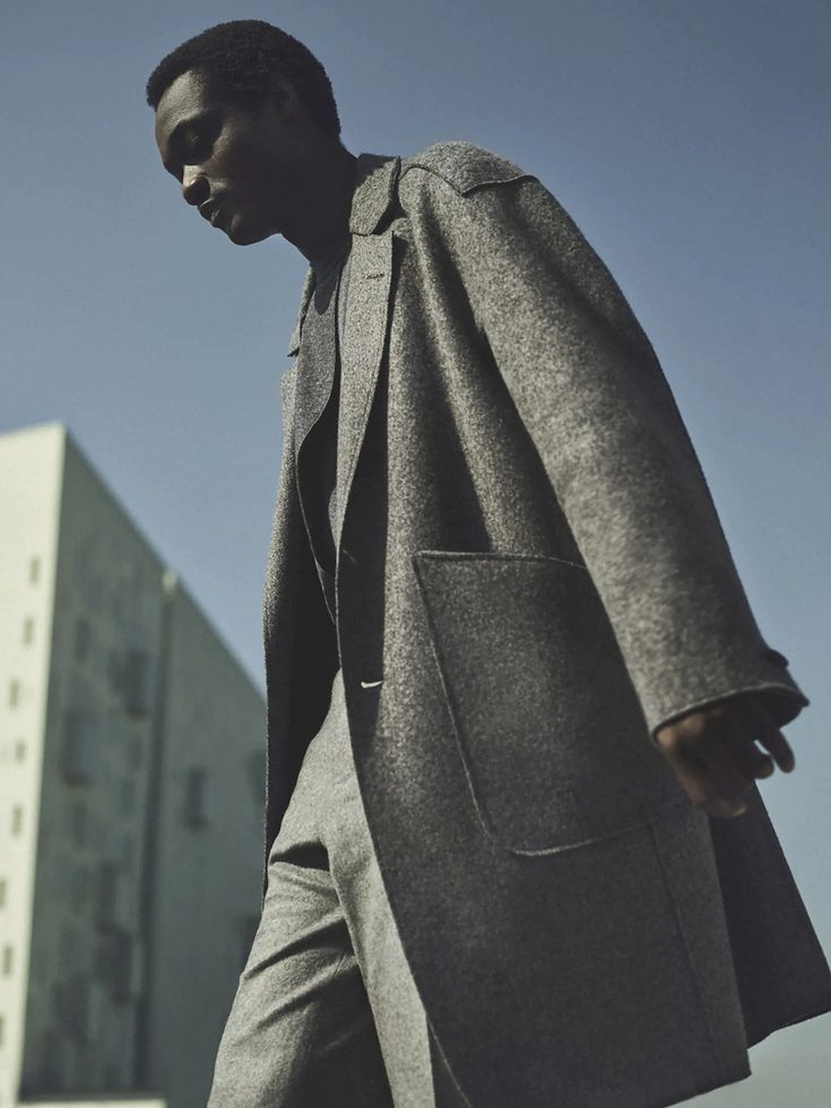 Man in a long grey coat against a pale sky