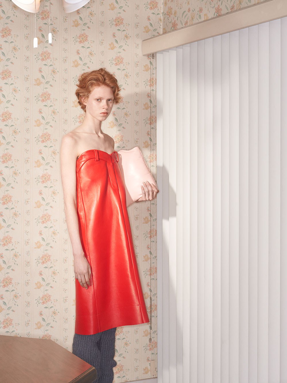 Model in a bright red strapless dress against floral wallpaper