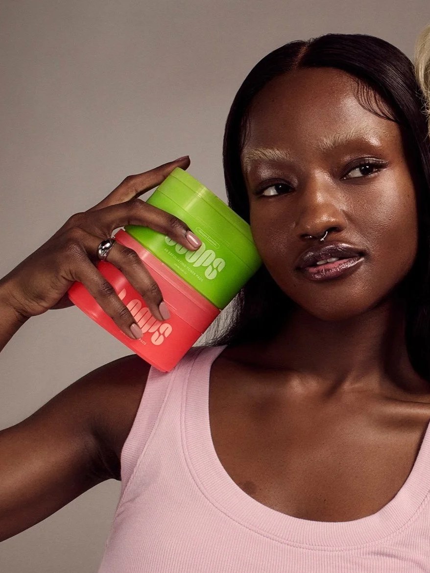 Black model in a pink tank top holding colorful LOOPS mask packs against a gray studio backdrop