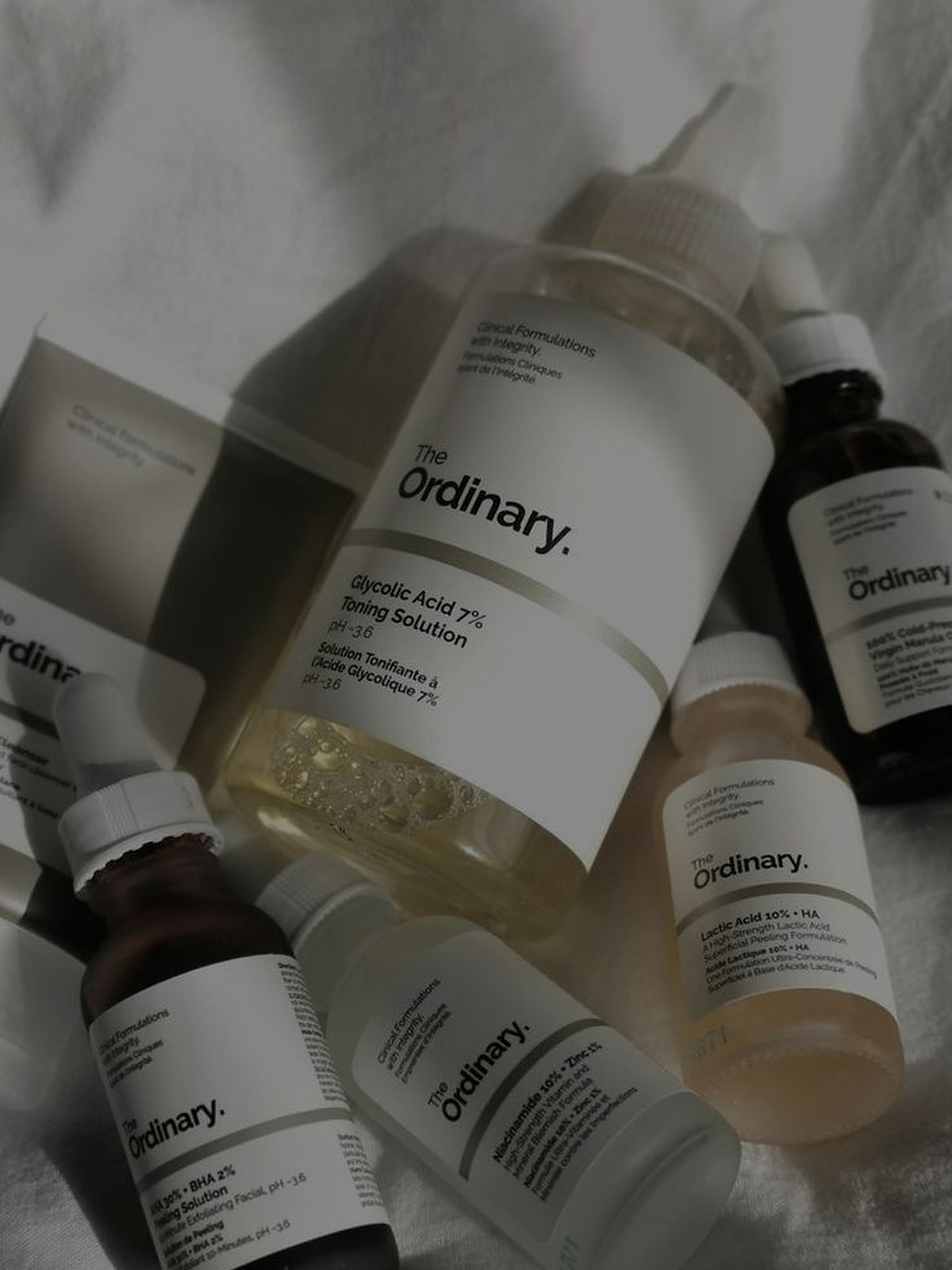 Overhead view of The Ordinary serum and cleanser bottles on white bedding