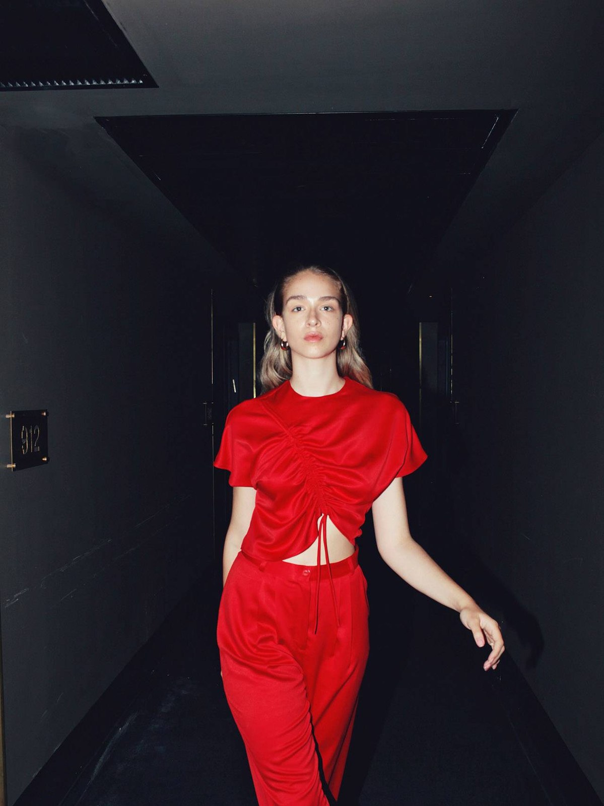 Model in a red cutout outfit walking through a dark corridor