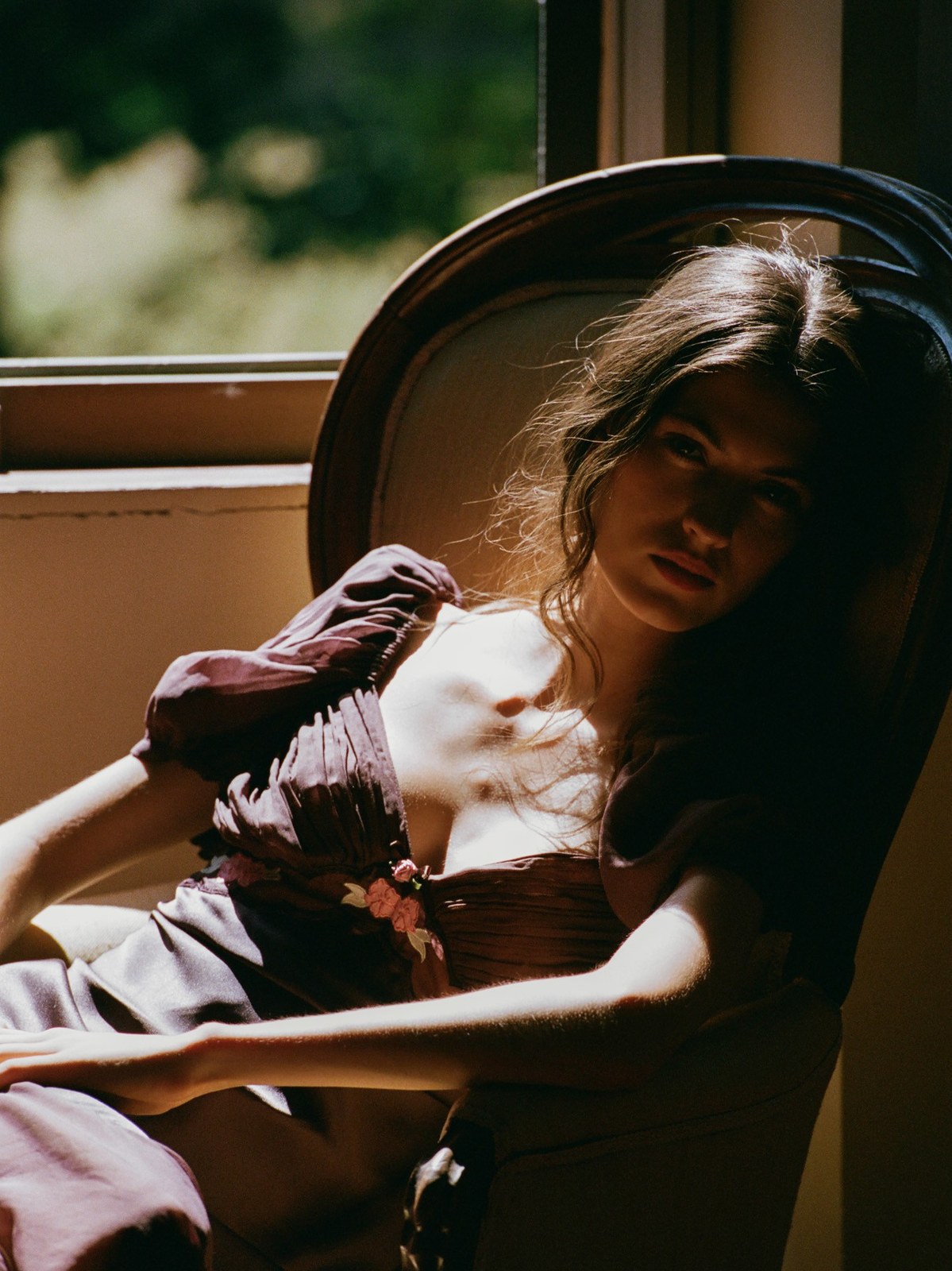 Model reclining in a mauve dress beside a window in soft shadow