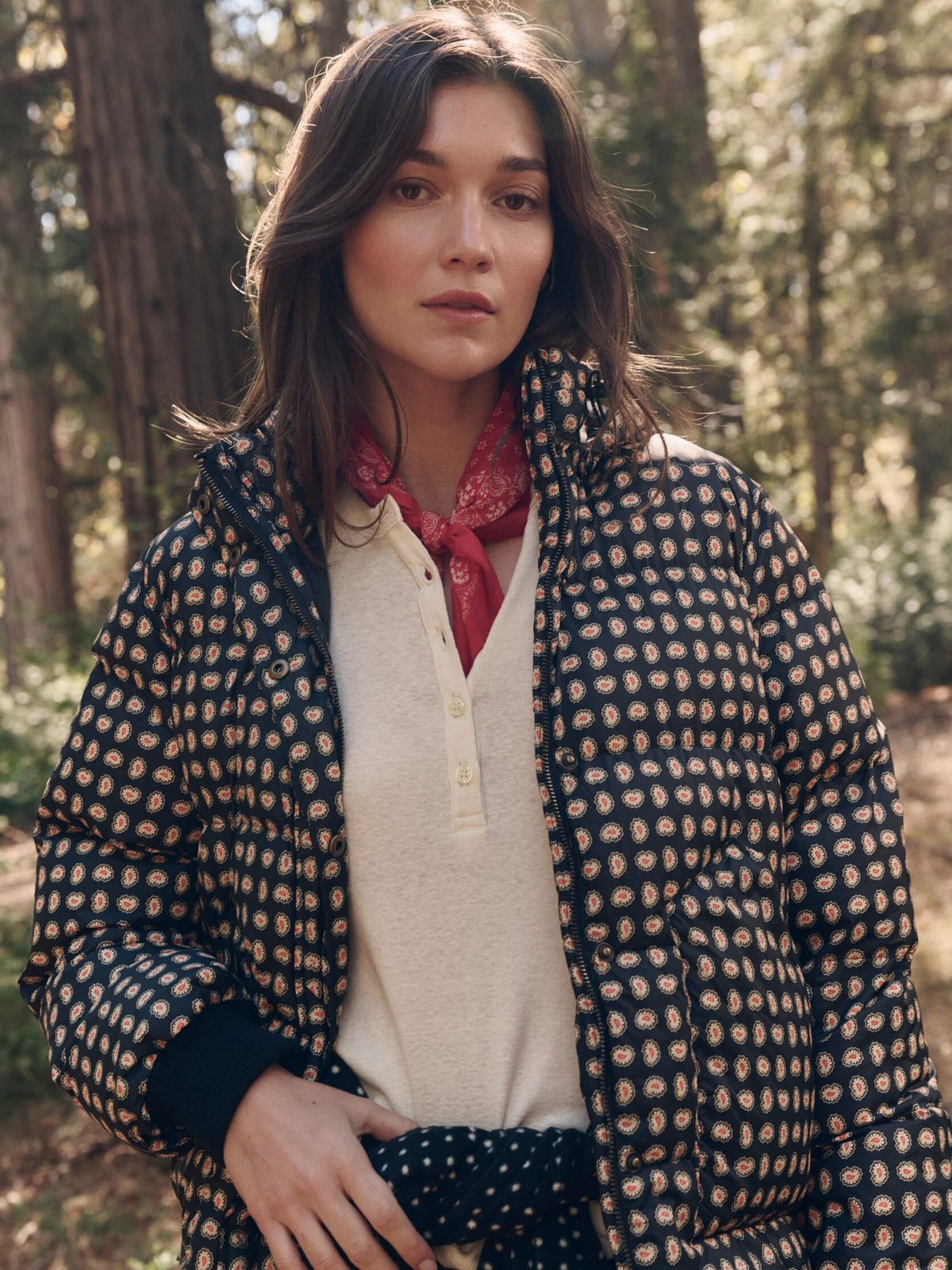 Model in a black paisley puffer with a red neck scarf in the woods