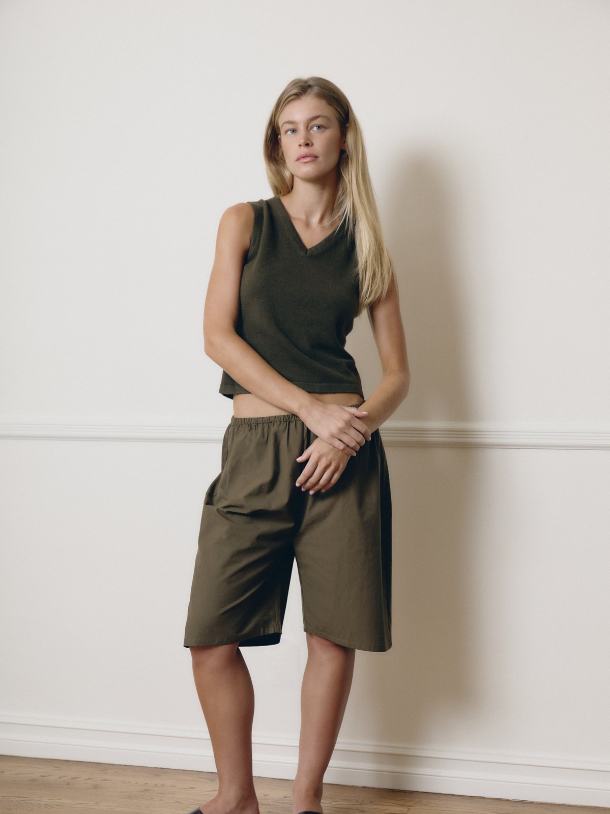Model in an olive sleeveless top and relaxed shorts in a pale studio