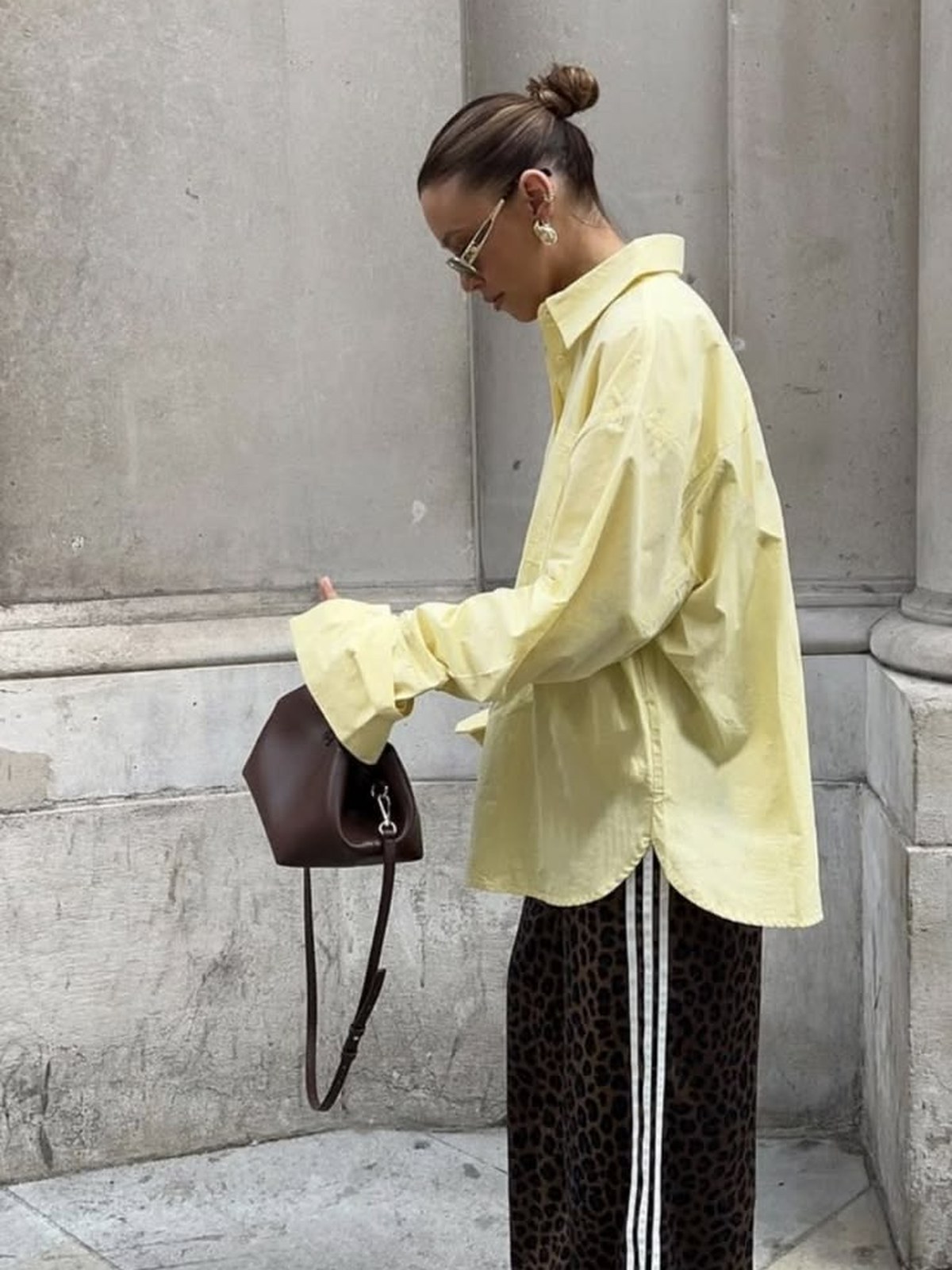Model in an oversized yellow shirt and striped trousers on a city street