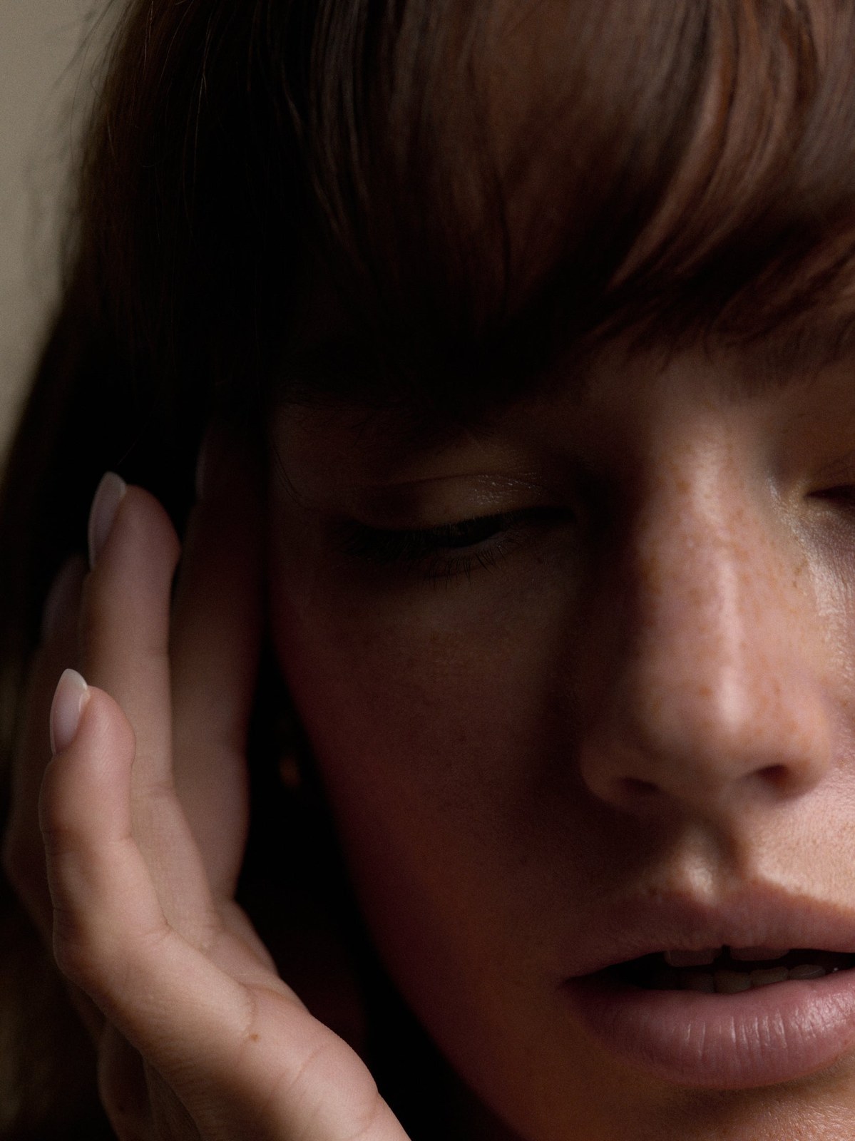 Model touching her cheek in a shadowed, intimate skincare portrait
