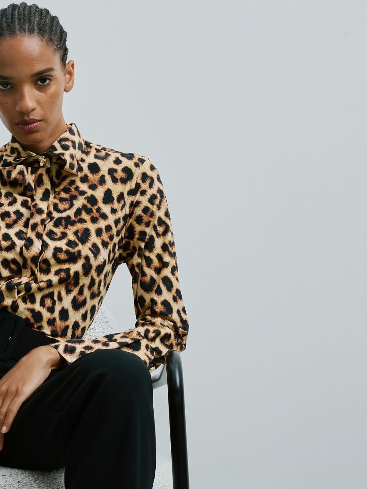 Model seated on a stool in a leopard print blouse and black trousers