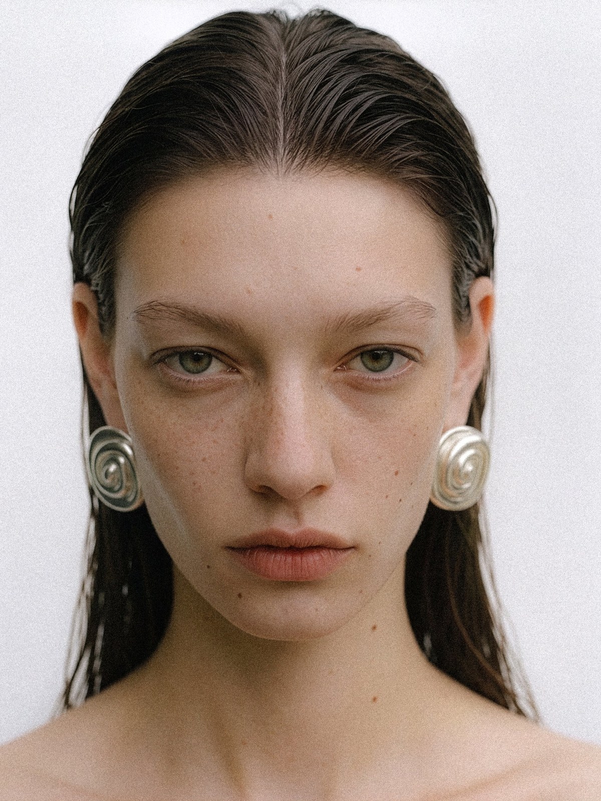 Model wearing oversized silver earrings in a pale studio portrait