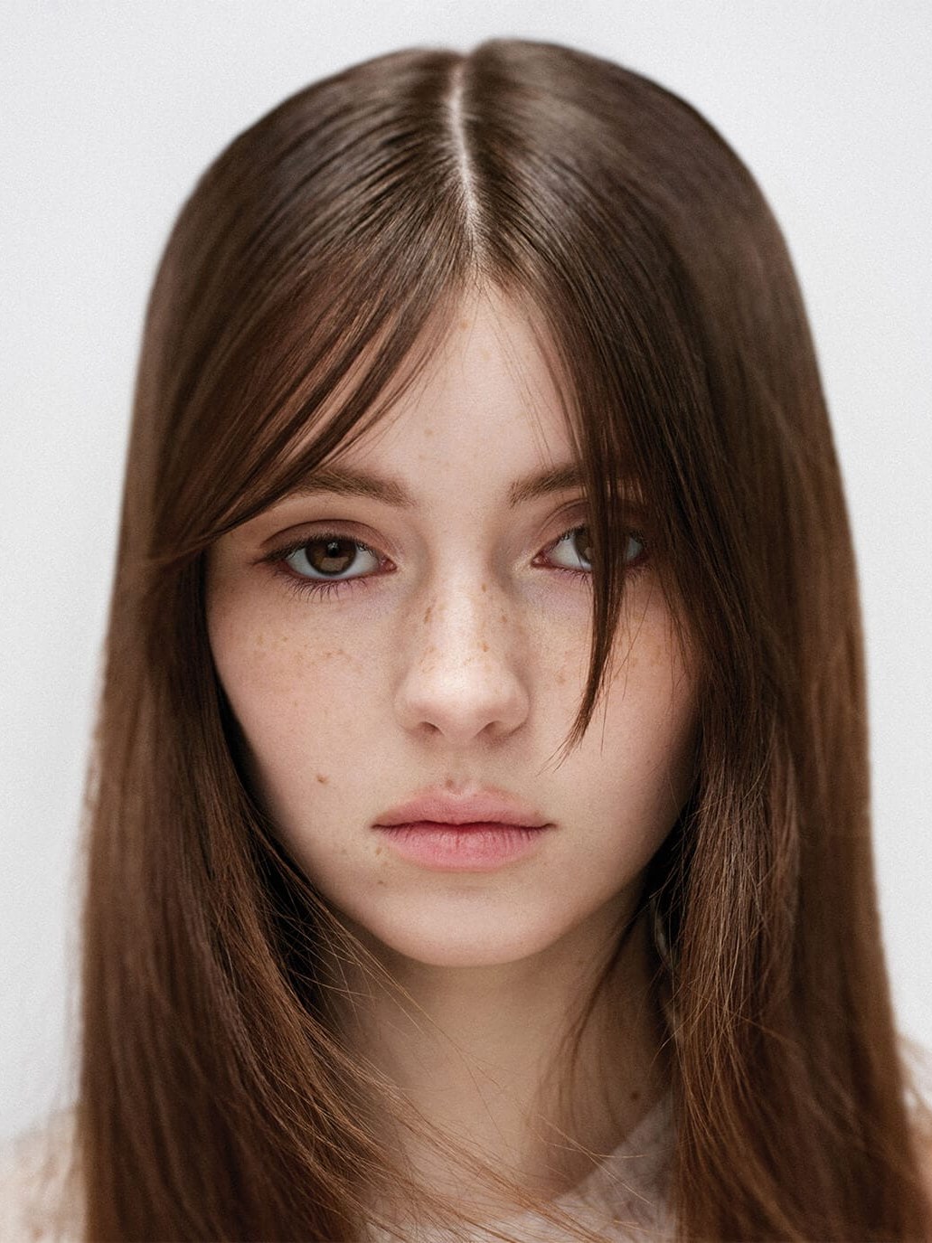 Freckled model with long brown hair in a pale studio portrait
