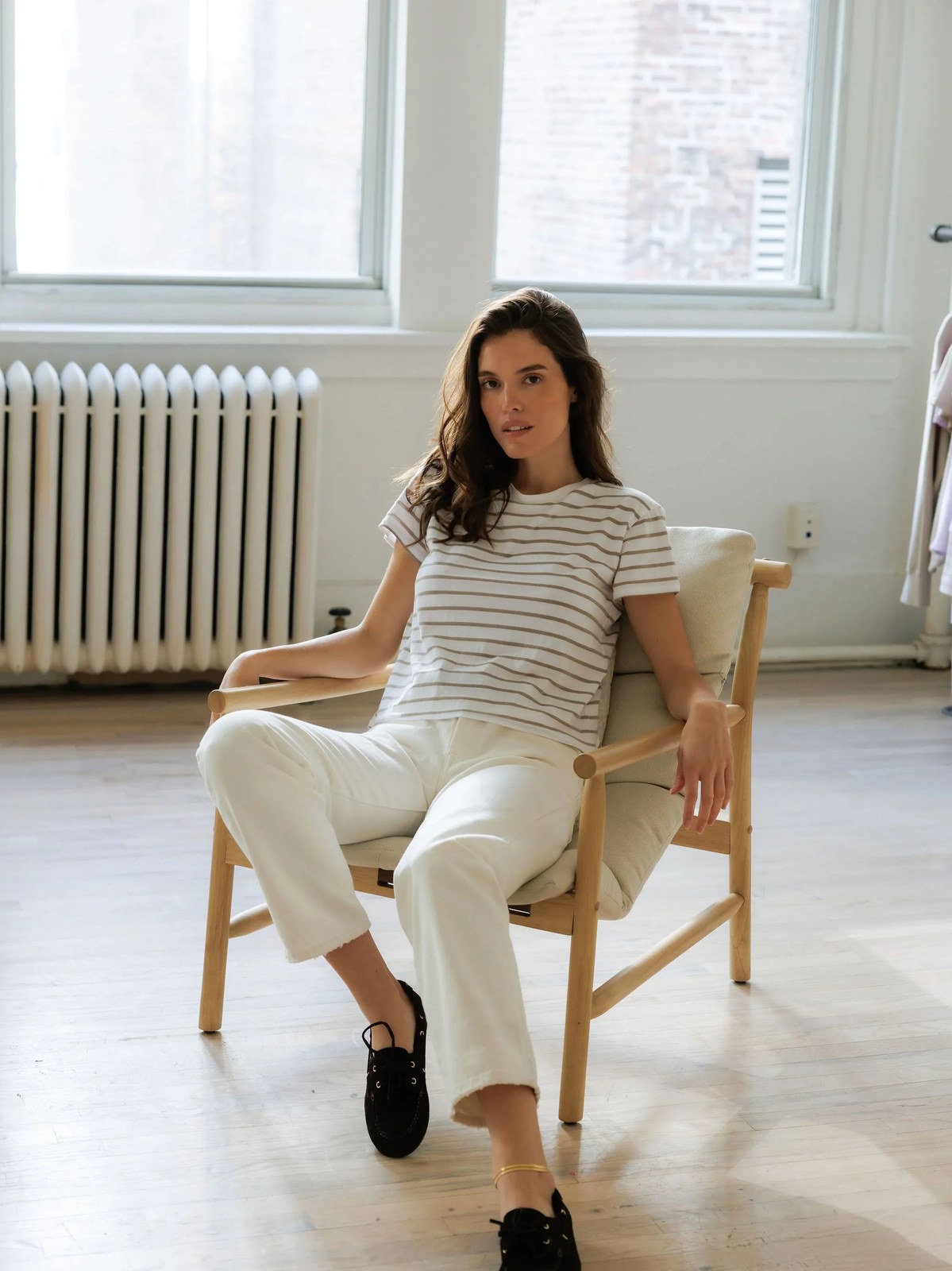 Woman in a striped tee seated in a chair beside a tall window