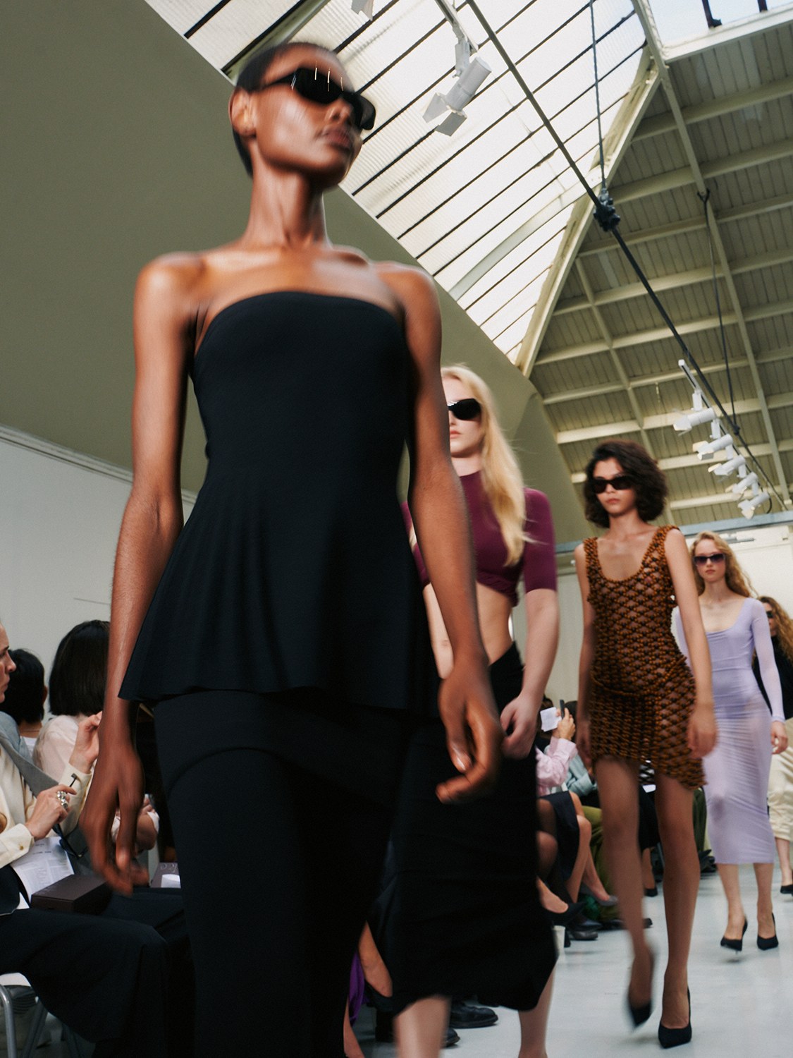 Models wearing sunglasses on a runway, with a lead model in a black dress